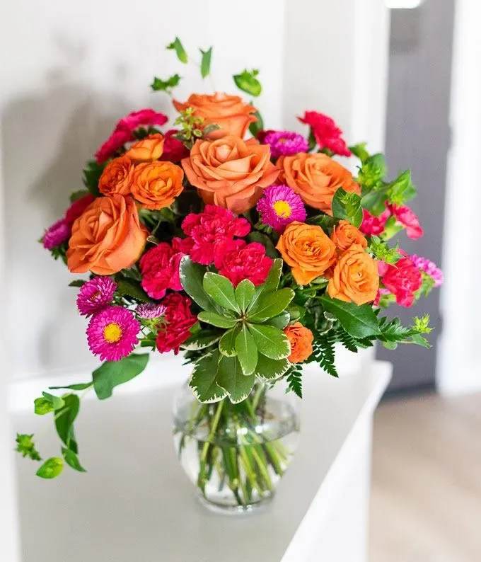 Orange roses and pink flowers arranged in a clear glass vase