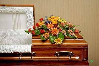 Colorful floral spray on a wooden casket beside a white quilted lining