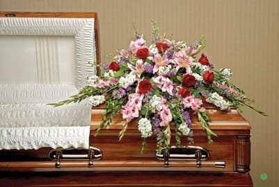 Floral spray on a wooden casket with pink, red, and white flowers