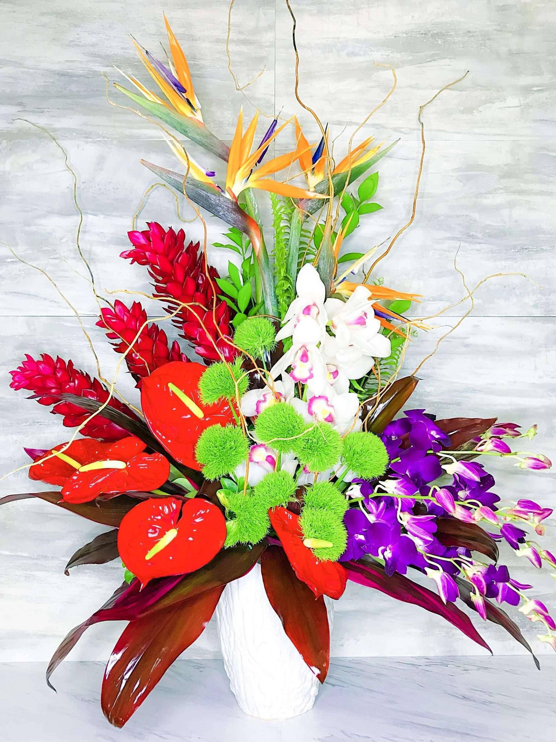 Tropical flower arrangement in a white vase with orchids and red anthuriums