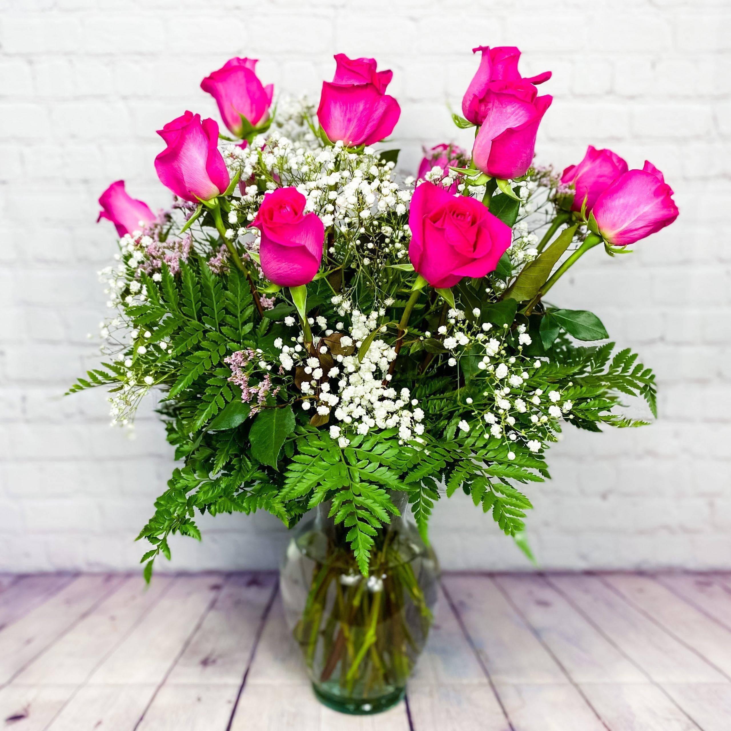 Pink roses arranged in a glass vase with baby's breath and fern