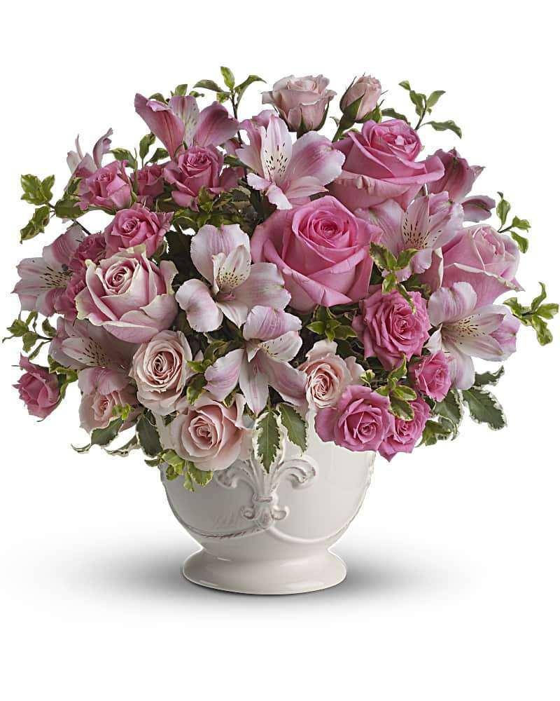 Pink roses and lilies arranged in a white urn vase