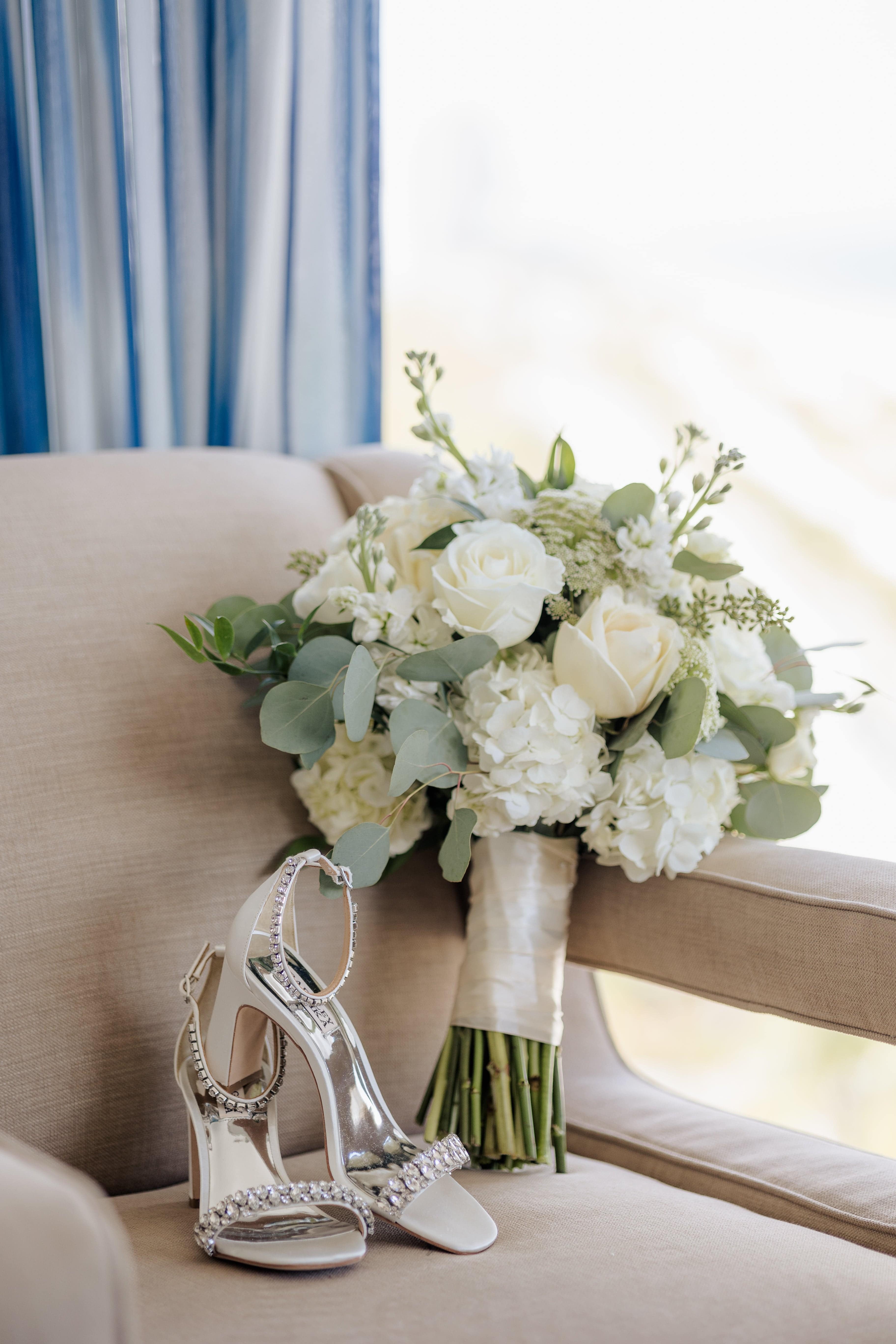 White rose bouquet with greenery beside jeweled high-heeled sandals