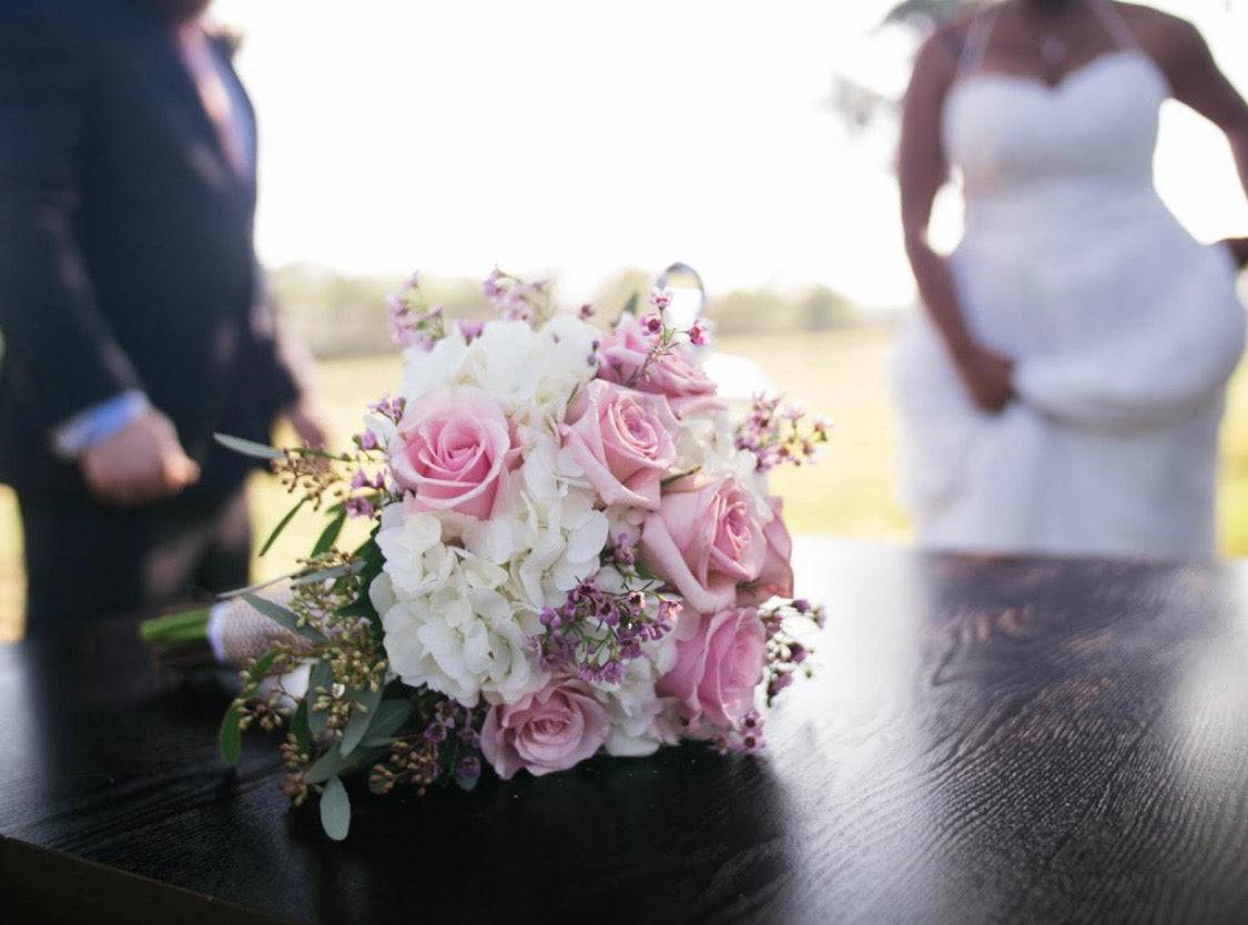 Pink and white bridal bouquet on a table with a bride and groom blurred in the background