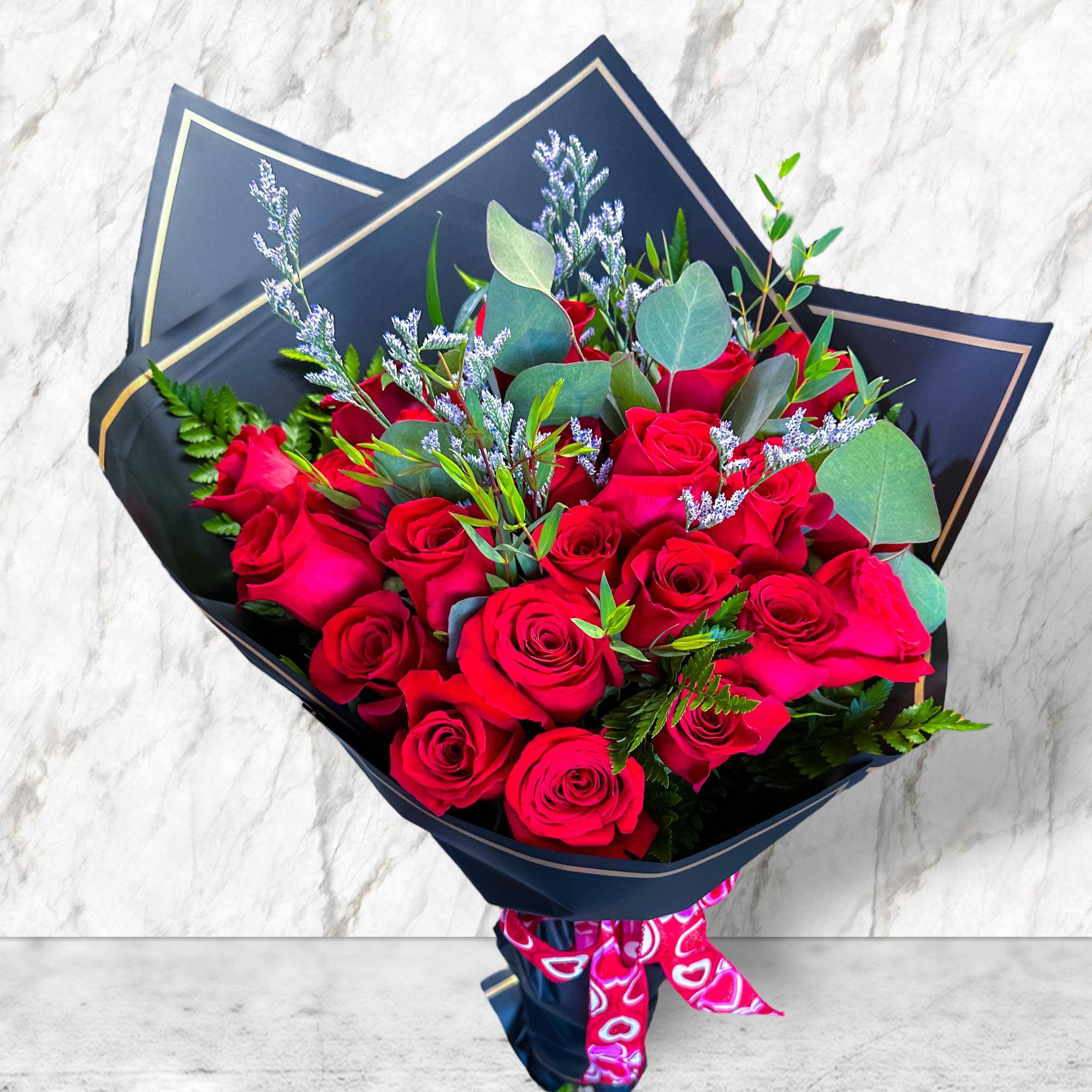 Bouquet of red roses wrapped in dark paper with a pink ribbon