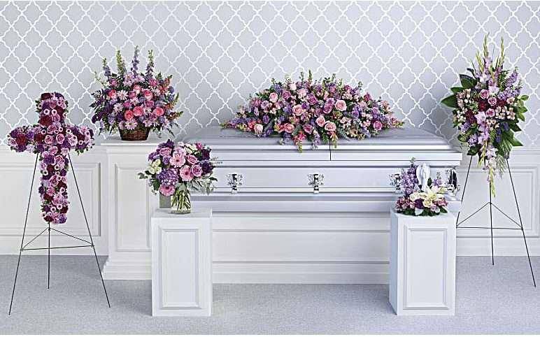 Floral casket spray and standing arrangements in pink and purple around a white casket