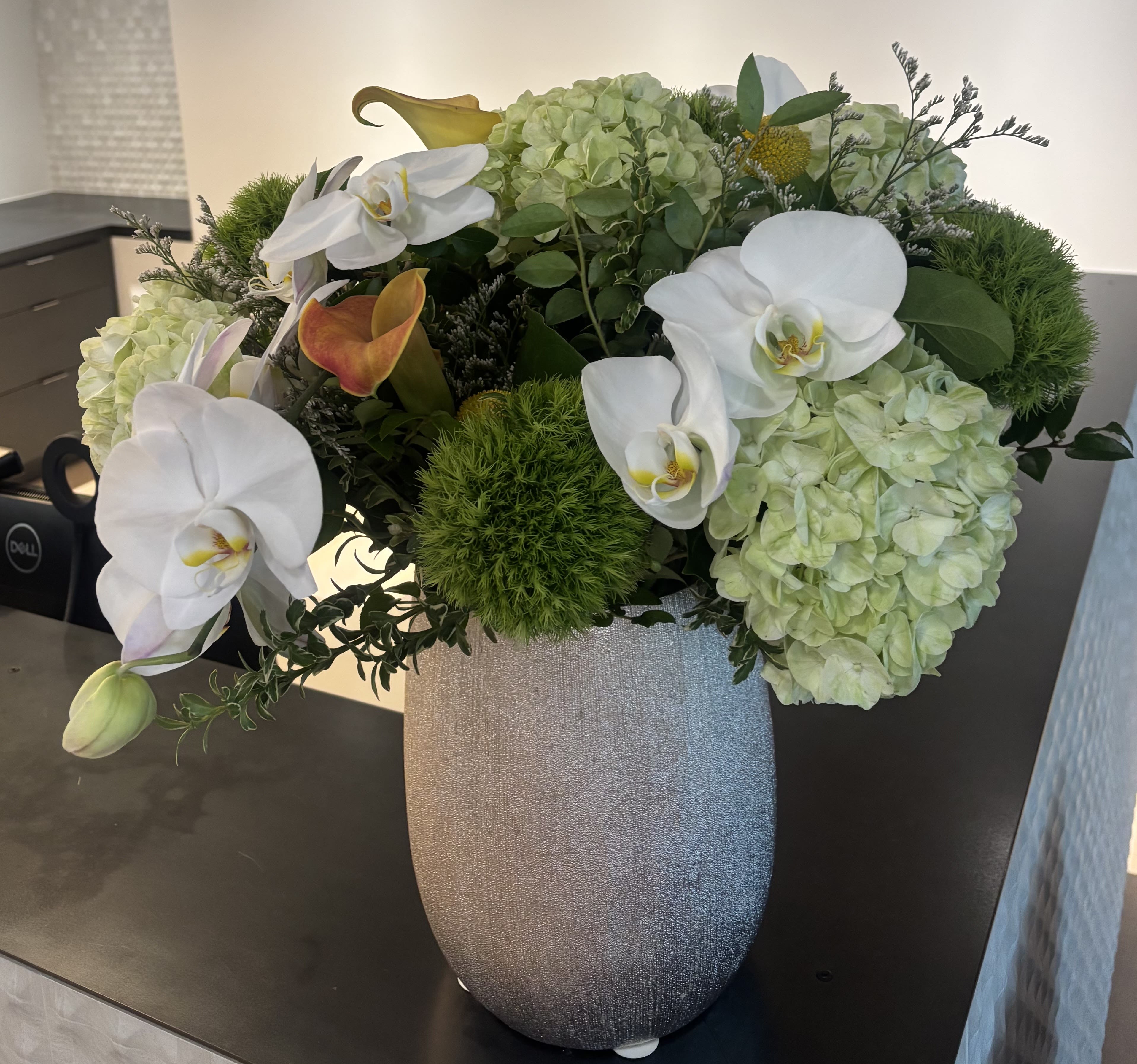 White orchids and pale green hydrangeas in a silver vase