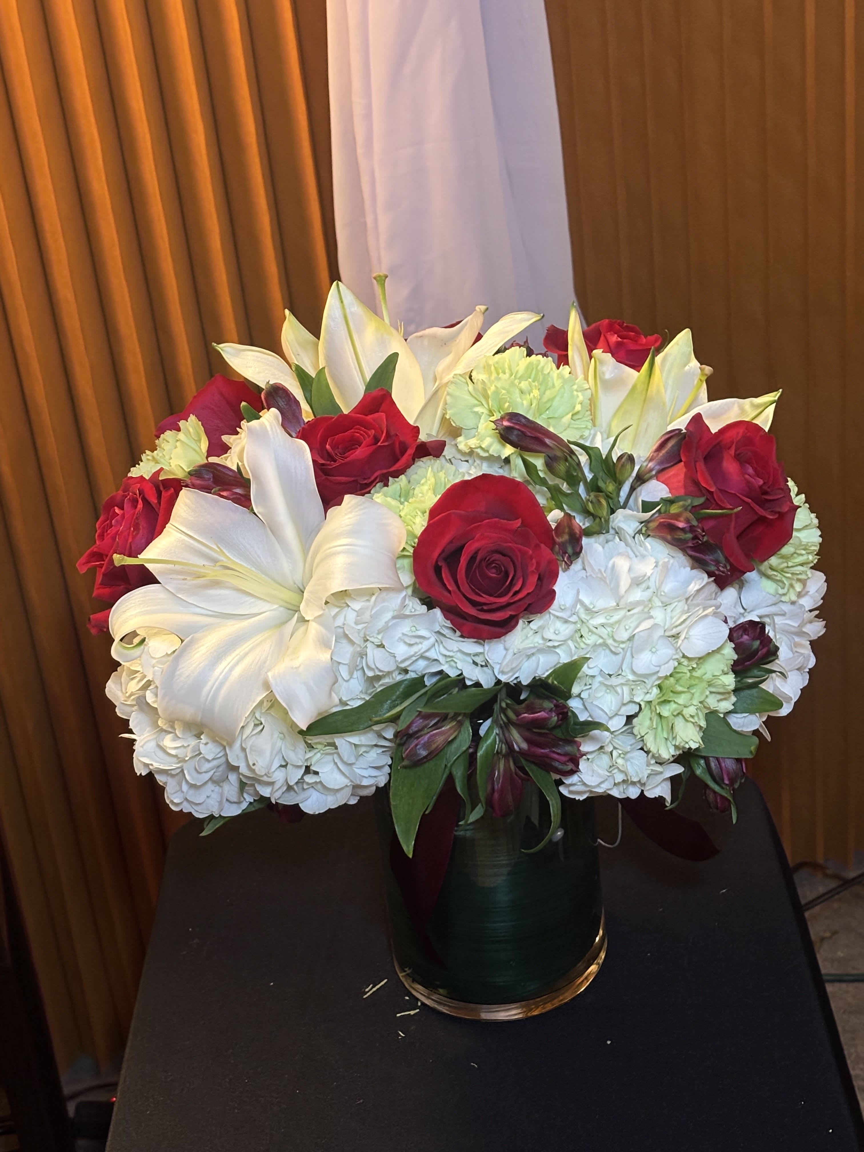 Bouquet of red roses, white lilies, and pale hydrangeas in a glass vase