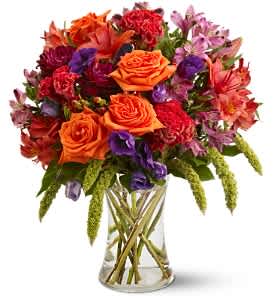 Mixed bouquet of orange, red, and purple flowers in a clear glass vase