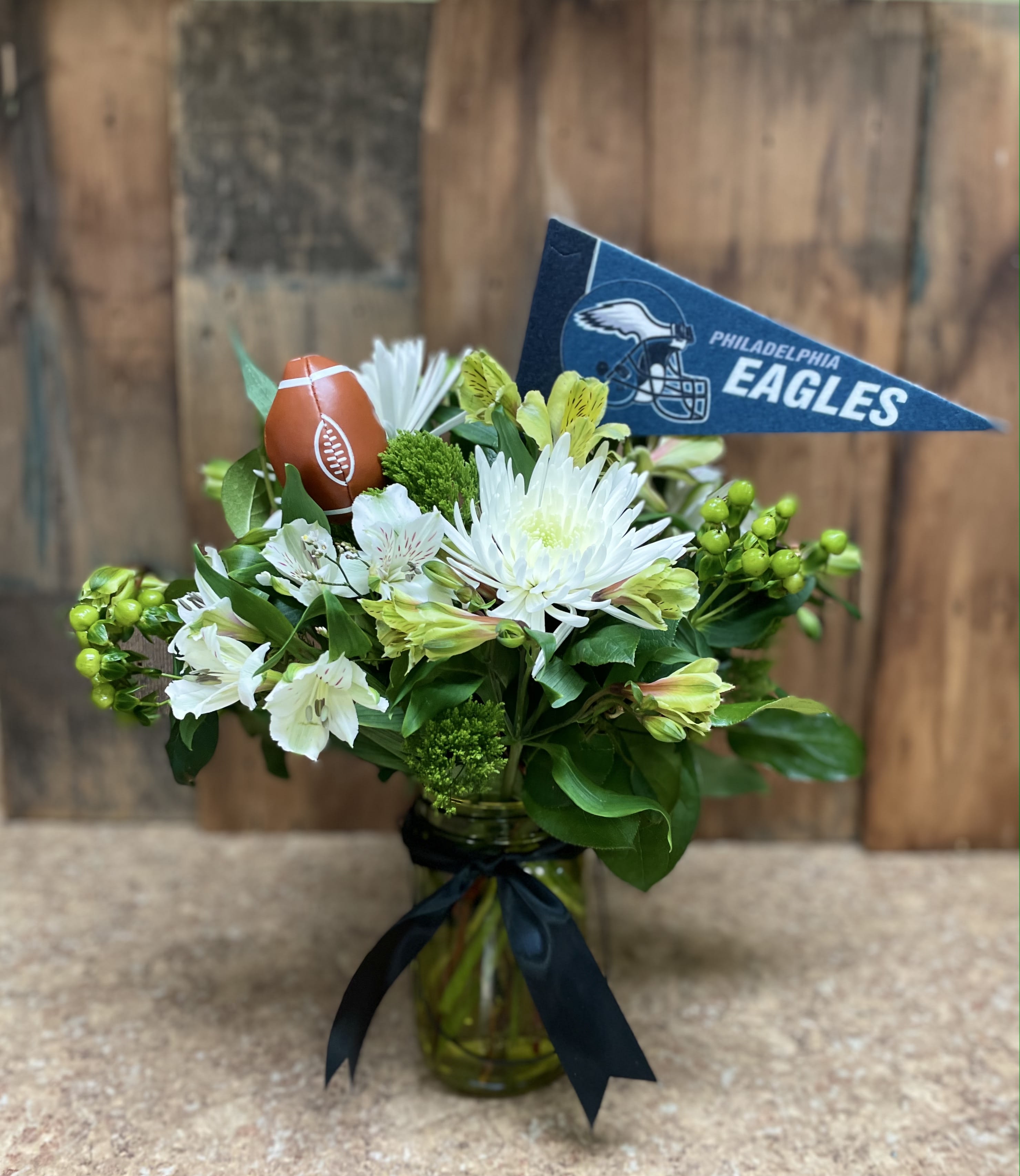 White flowers in a glass vase with a Philadelphia Eagles pennant and football decoration