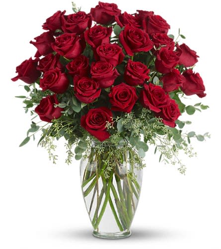 Red roses arranged in a clear glass vase with greenery