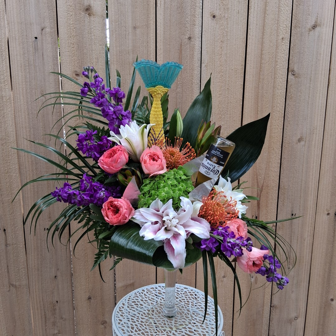 Tropical floral arrangement in a clear pedestal vase with purple and pink blooms