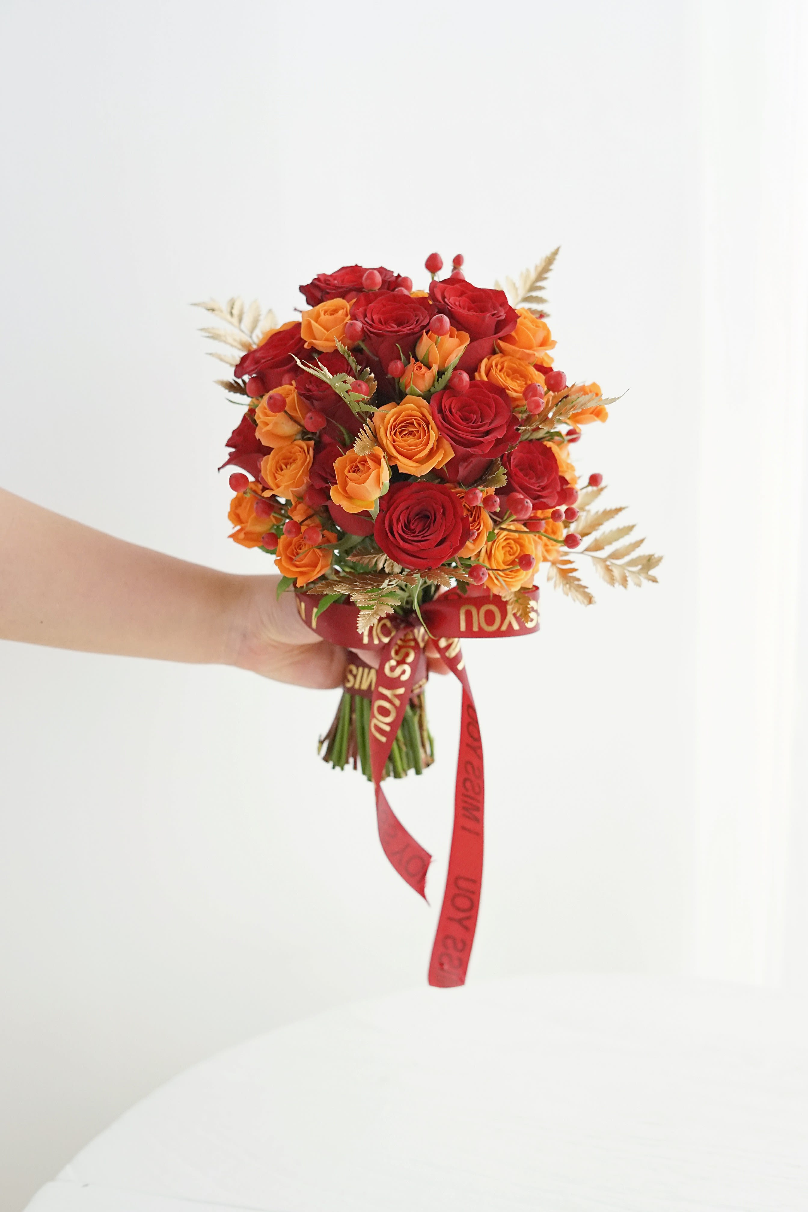 Handheld bouquet of red and orange roses with a red ribbon