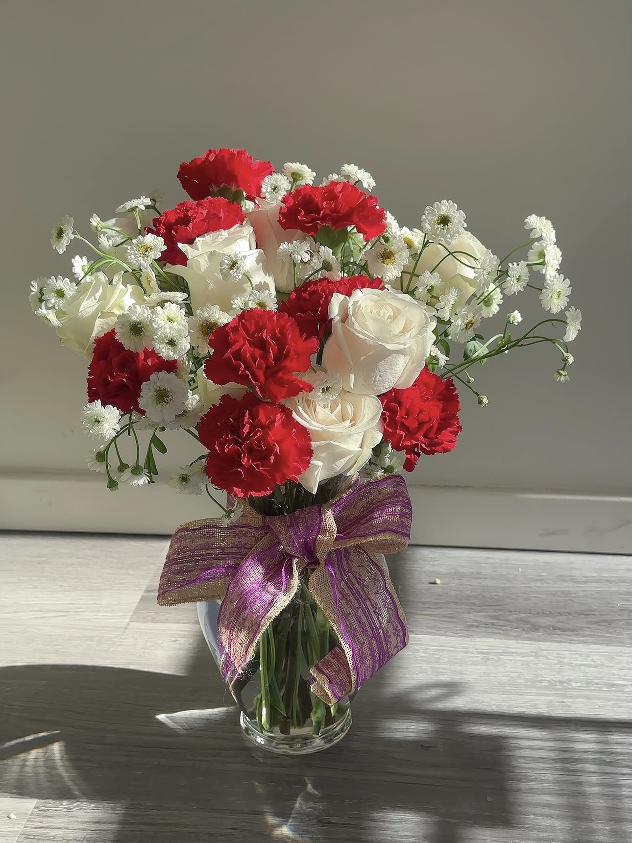 Bouquet of red carnations and white roses in a glass vase with a purple ribbon