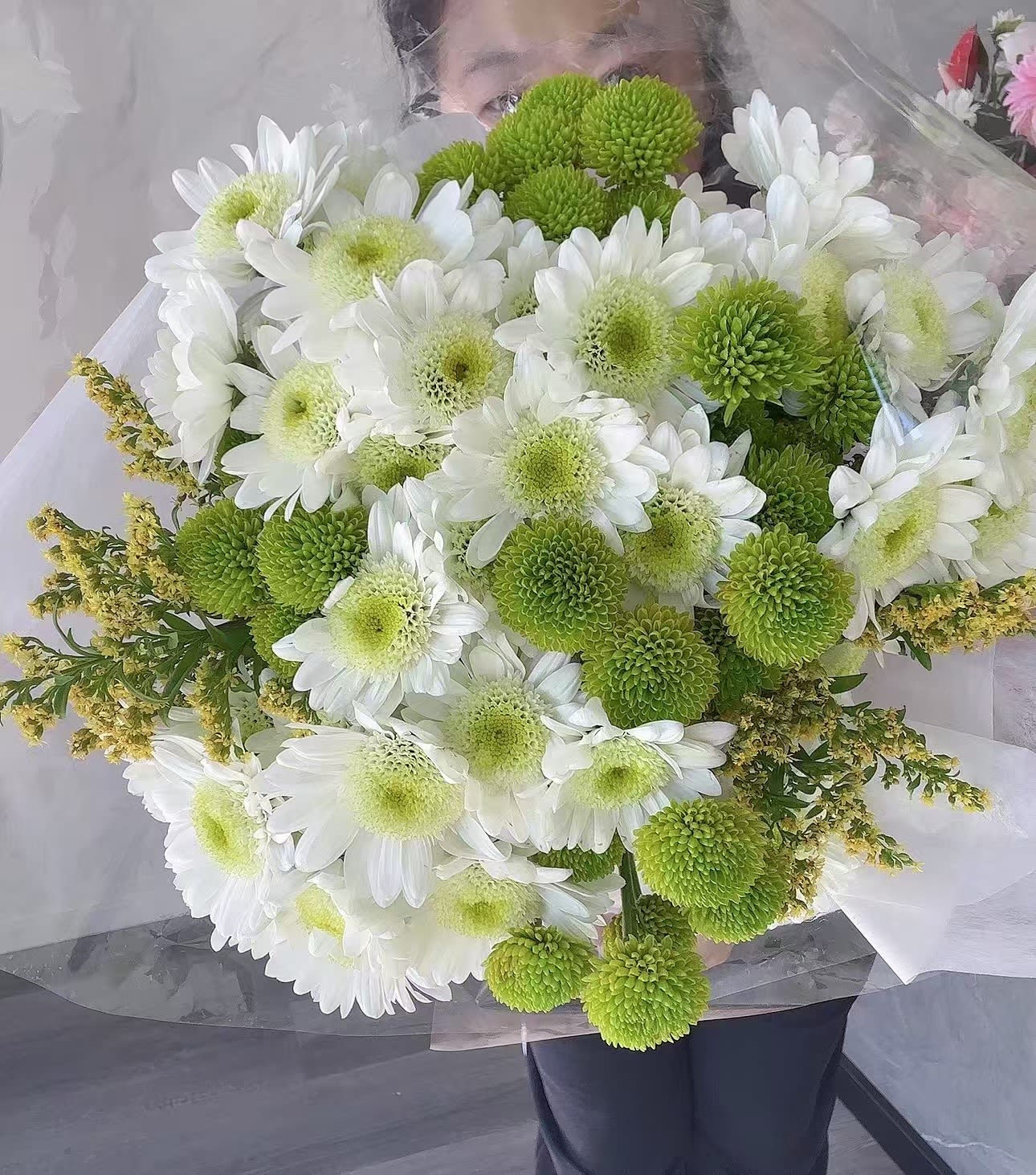 Bouquet of white daisies and green pompon chrysanthemums wrapped in clear paper