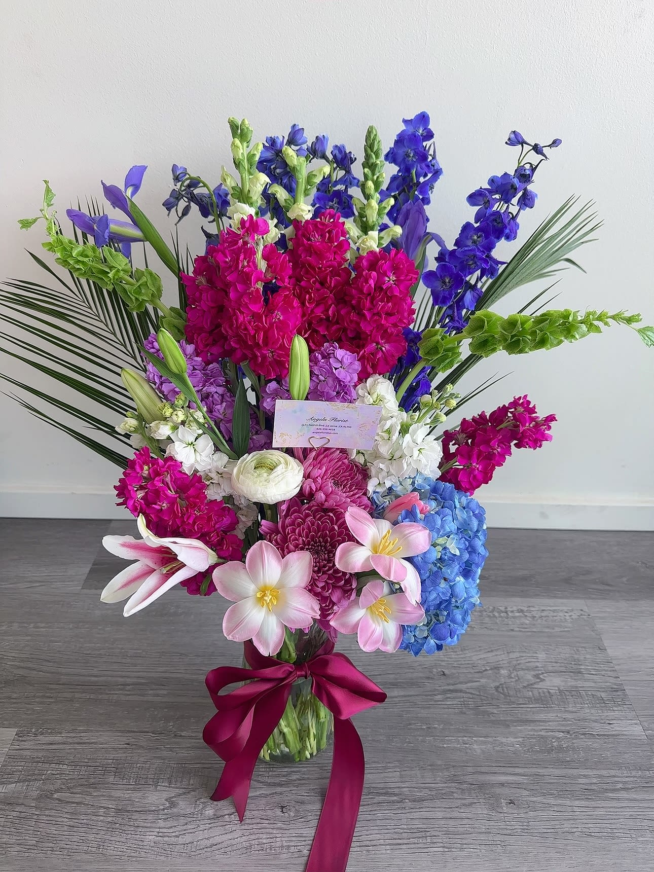 Tall bouquet of pink, blue, purple, and white flowers in a glass vase