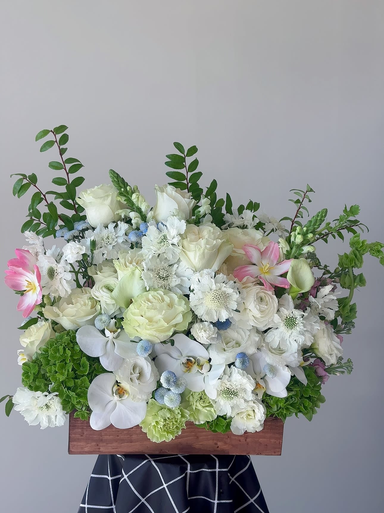 White floral arrangement with orchids and roses in a wooden box