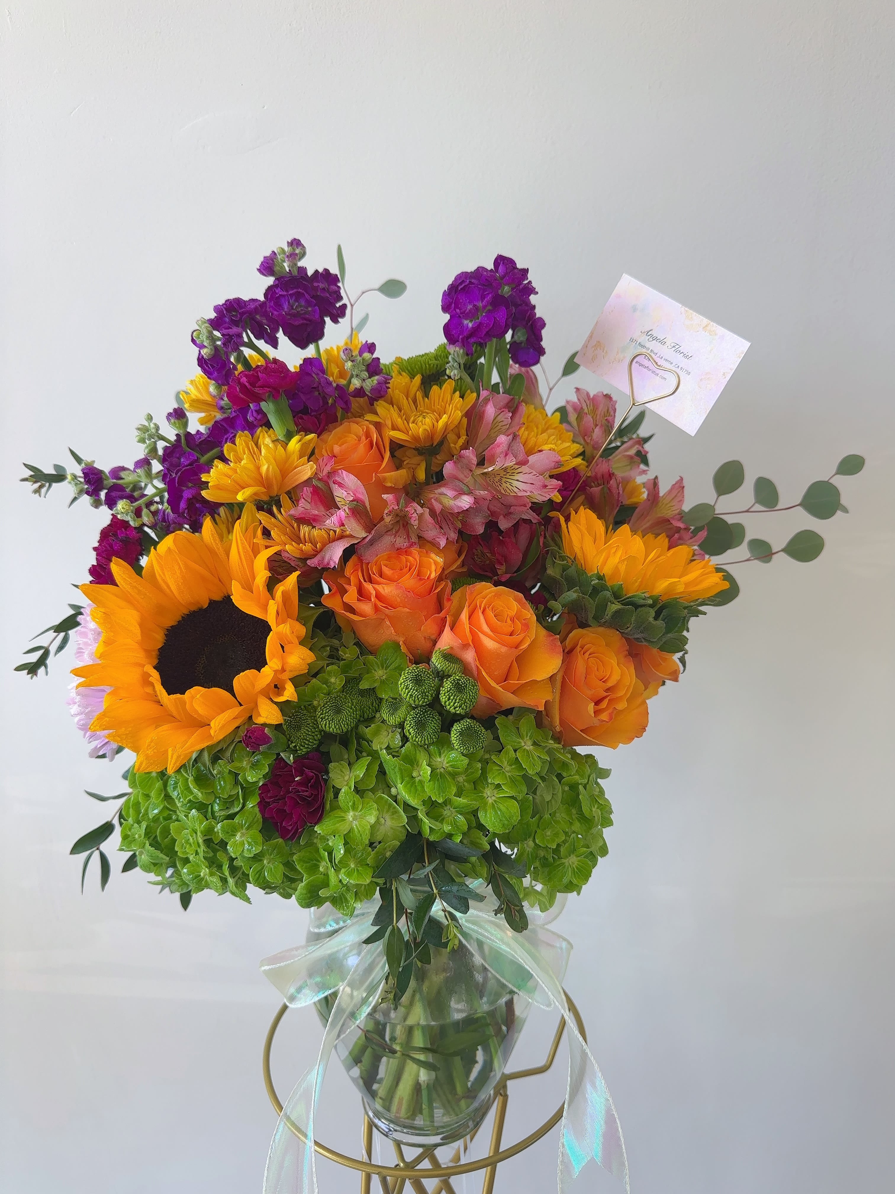Bouquet of sunflowers, orange roses, and purple blooms in a glass vase