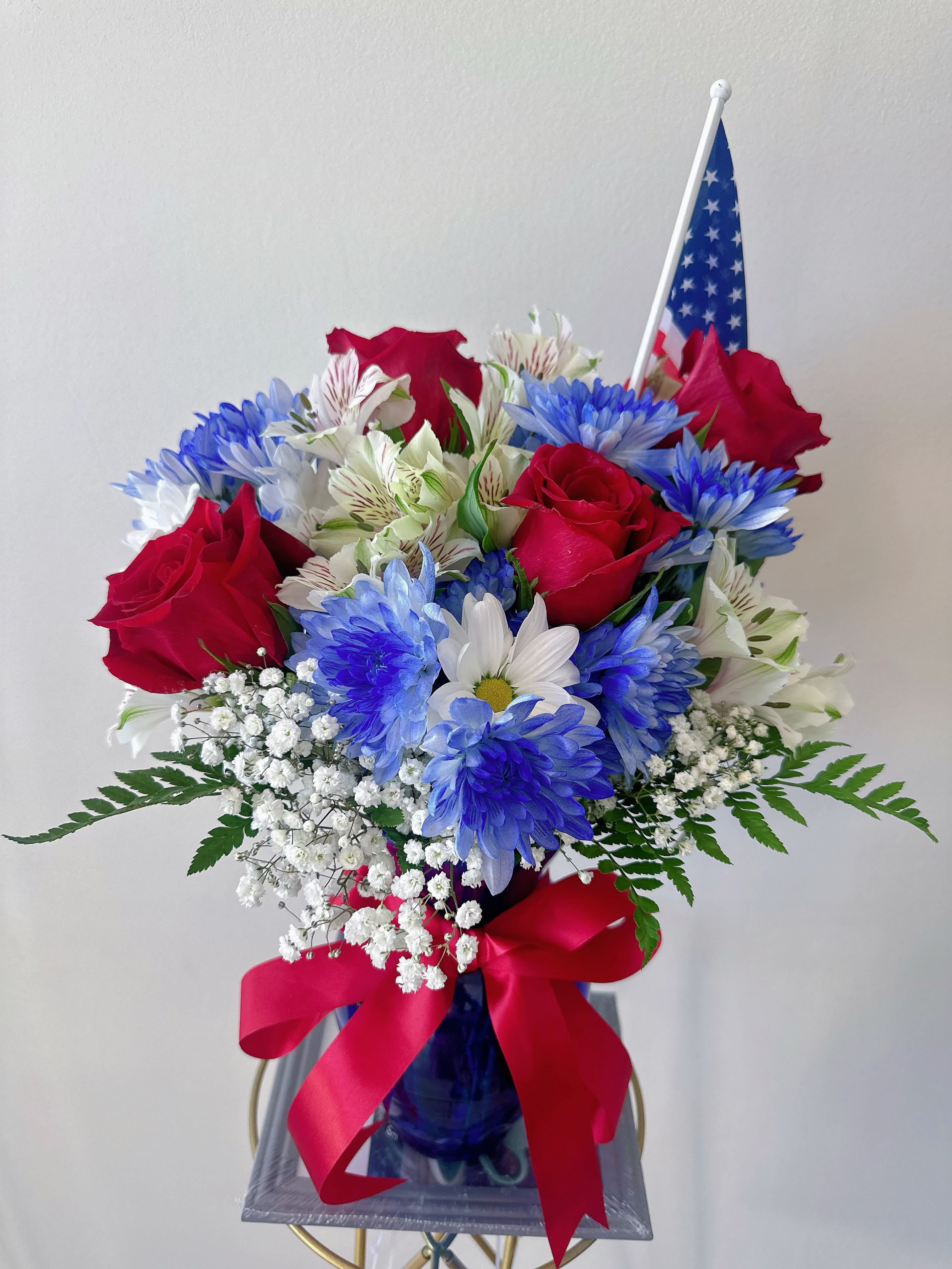 Bouquet of red roses, blue and white daisies, and baby's breath in a blue vase