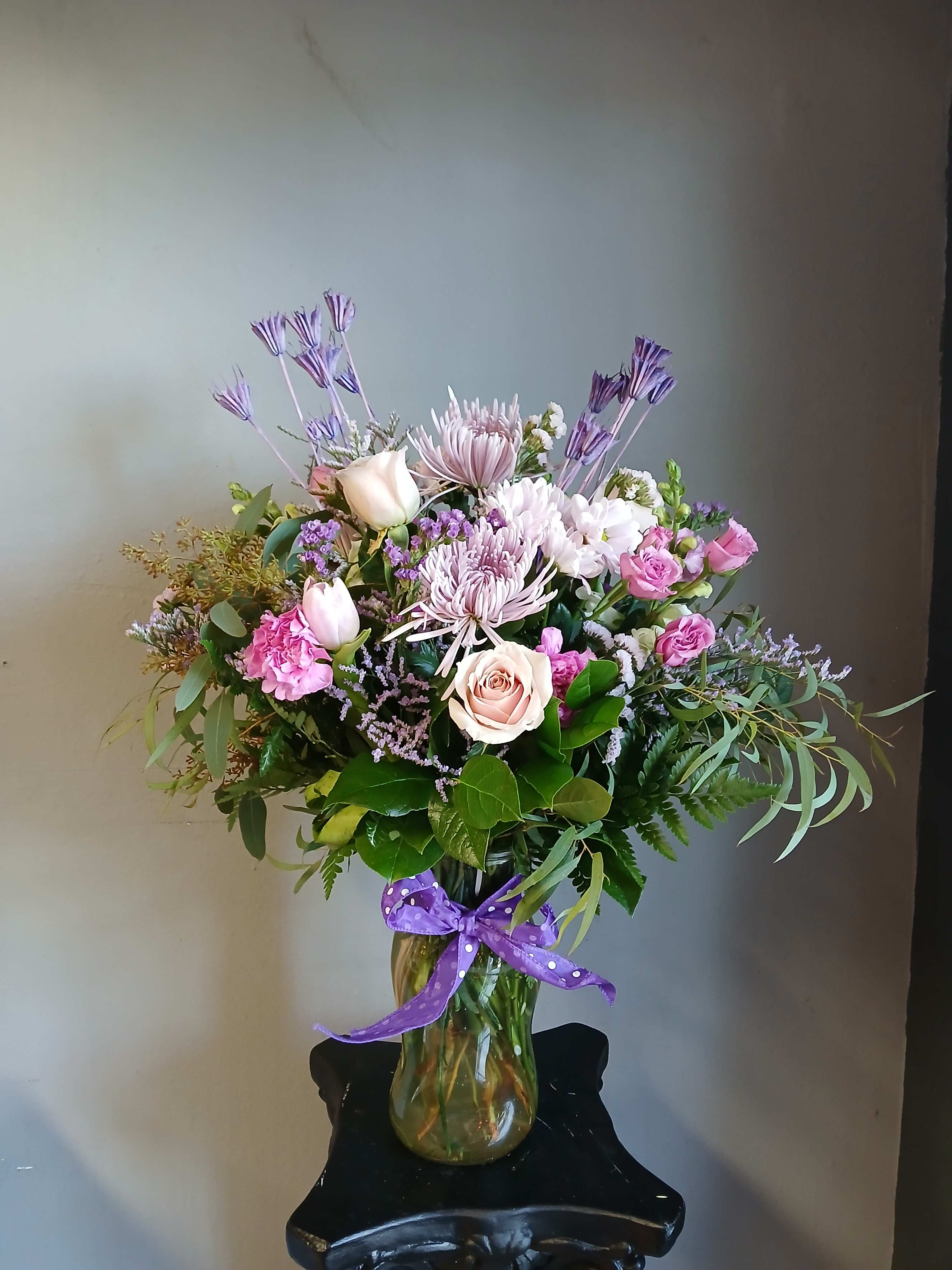 Mixed pink and lavender bouquet in a glass vase with a purple ribbon.