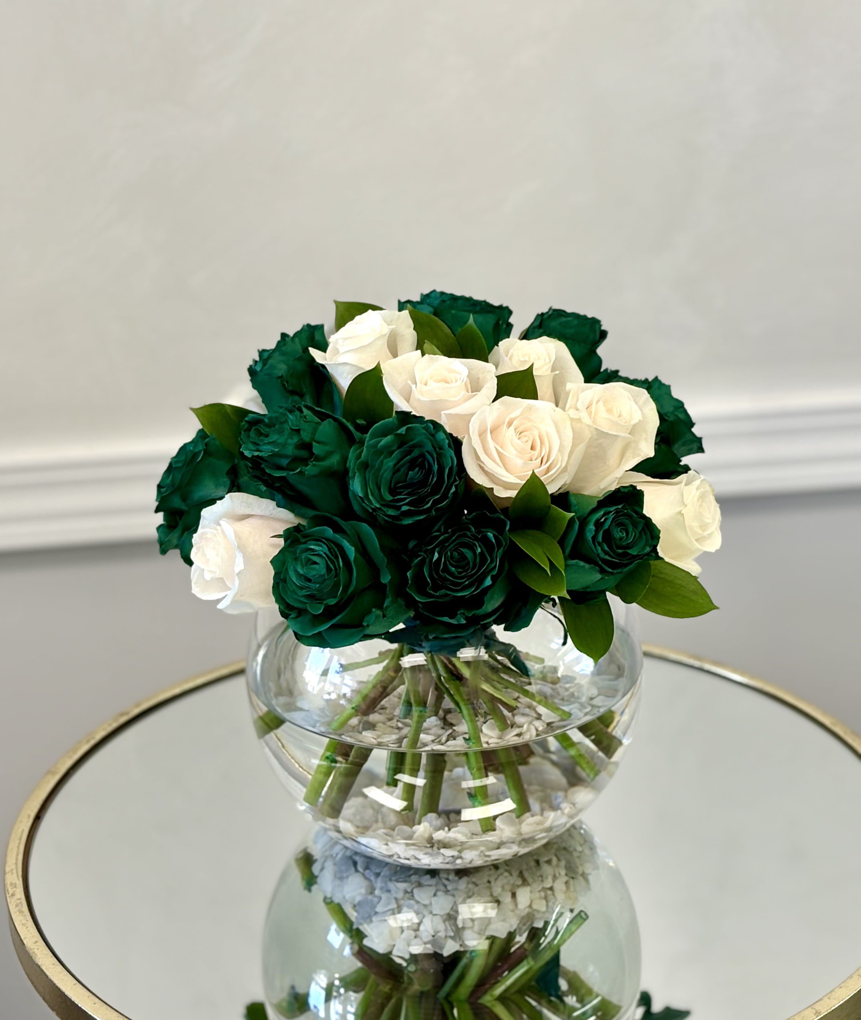 Green Velvet Rose Garden By VLM Flowers - Deep green roses take center stage alongside delicate ivory roses, creating a rich and luxurious look. Set in a clear vase with subtle stone details, this arrangement brings elegance and a bold color contrast to any setting.