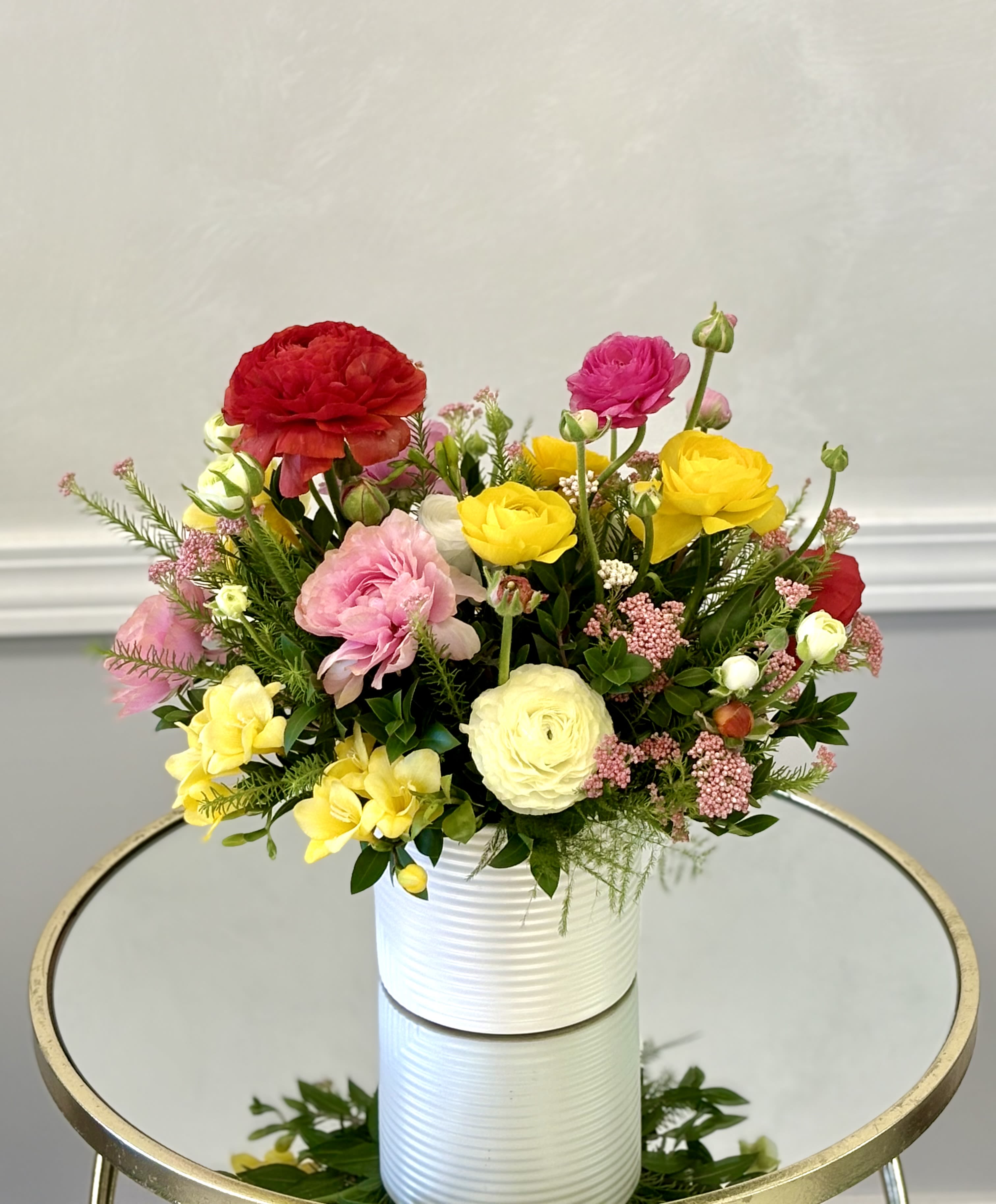 Garden Party Bloom By VLM Flowers - A bright mix of ranunculus, peonies, and seasonal blooms in a modern white vase, bringing a fresh, cheerful garden feel to any space.