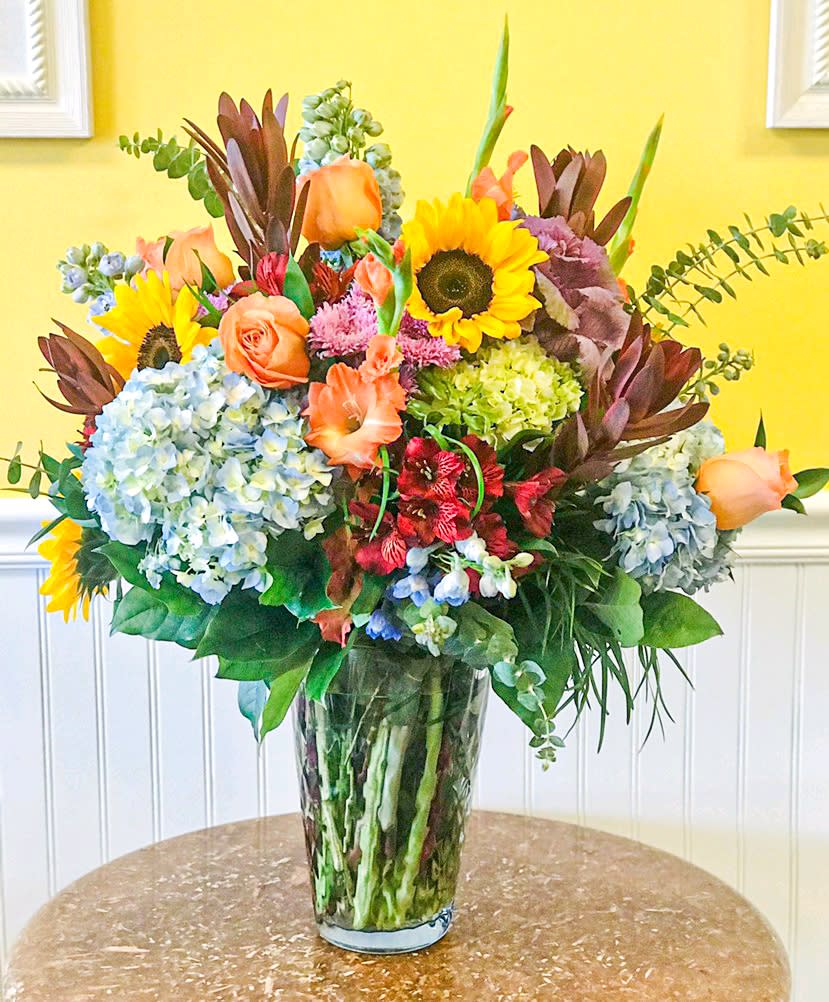 Mixed bouquet with sunflowers, roses, hydrangeas, and lilies in a glass vase