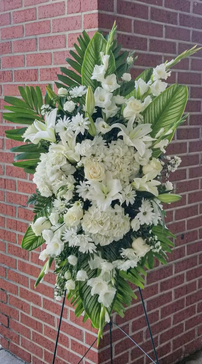 White funeral spray with lilies, roses, and daisies on an easel