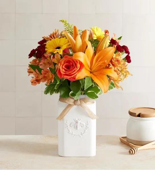 Honey Bee Buzz For Fall - Get them buzzing for fall! Our unique, stylized bouquet is gathered with a mix of blooms in warm yellow, orange, bronze and burgundy. Designed in our Sweet As Can Bee artisanal vase, featuring an adorable honey bee and raffia bow, it’s a gift that adds seasonal beauty to any decor.