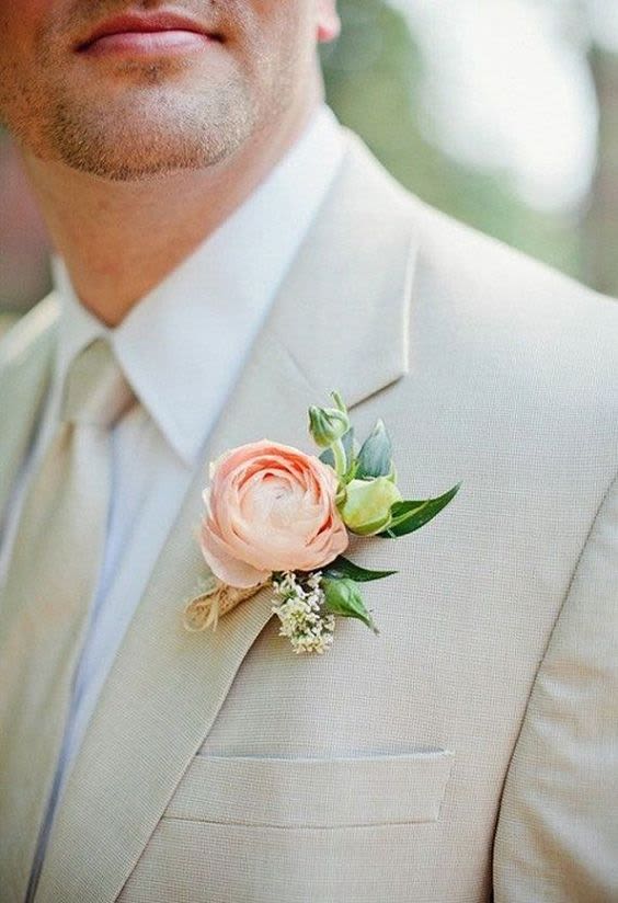 Boutonniere with a blush ranunculus on a beige suit lapel