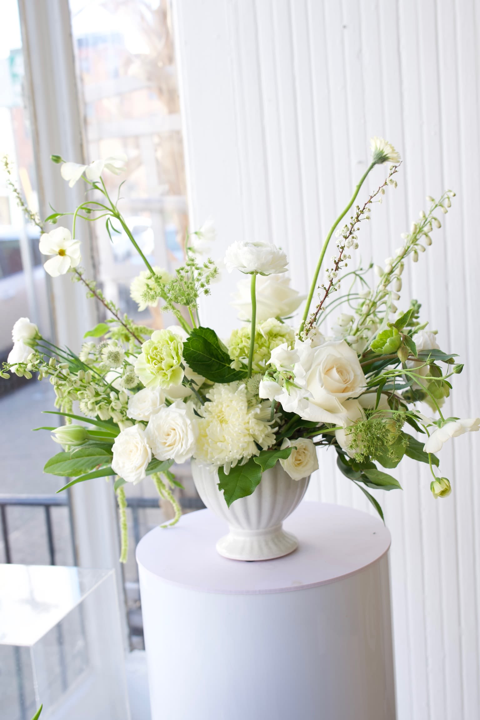 White floral arrangement in a white urn vase on a round pedestal