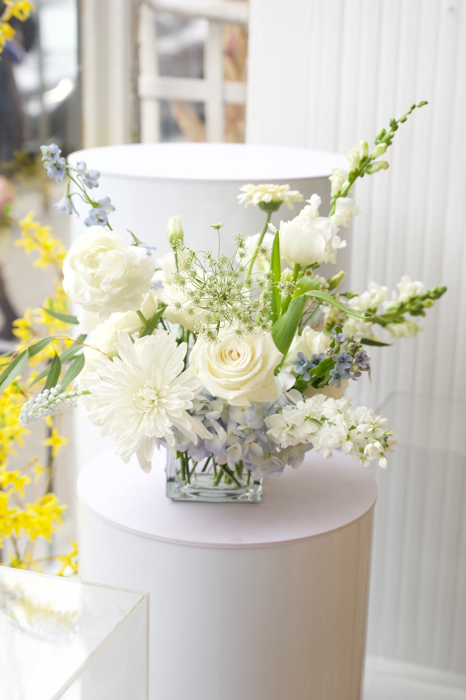 White floral arrangement in a clear square vase with blue accents