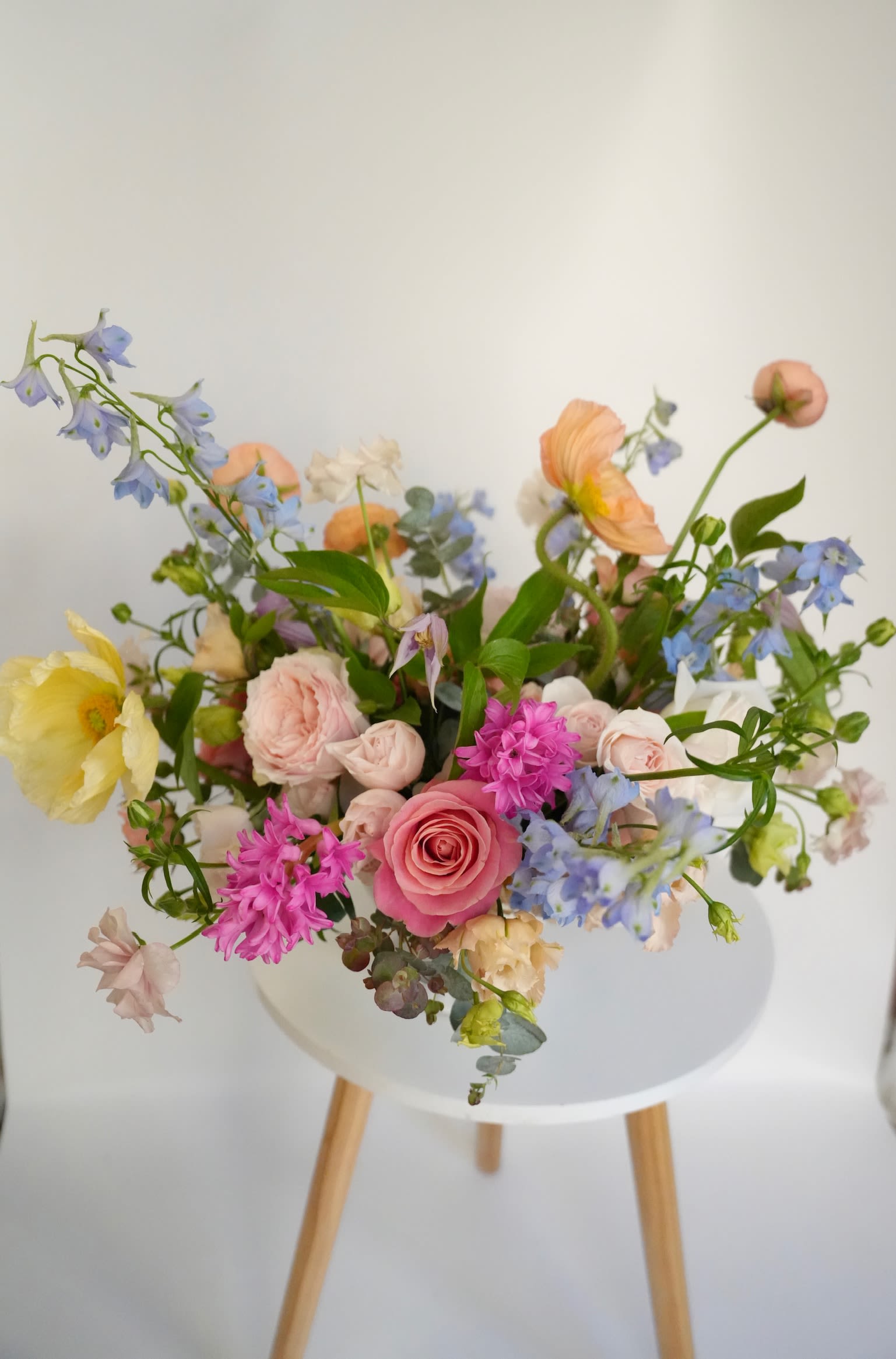 Spring Poetry - An airy garden arrangement filled with soft pastel blooms and delicate movement. Featuring roses, poppies, delphinium, hyacinth, and seasonal accents, this piece feels like a freshly gathered bouquet from a spring garden. Designed in our signature natural style, it brings softness, color, and a little poetry into any space.