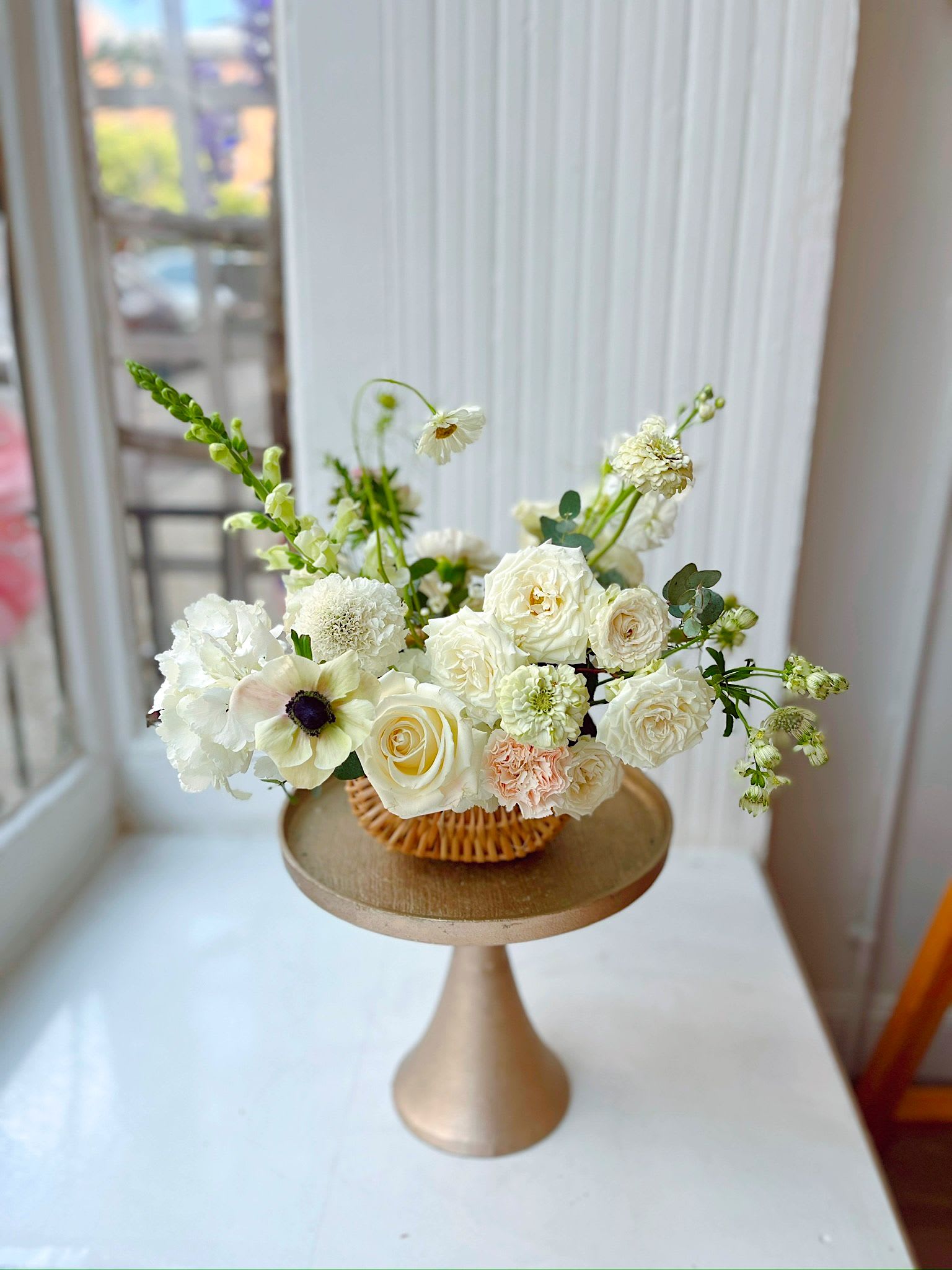 Bloomie Basket  - A fresh, garden-style flower basket filled with creamy white roses, seasonal blooms, and soft textural accents, arranged in a natural woven basket. Designed for an effortless, just-picked feel, this arrangement is perfect for everyday gifting, housewarmings, or brightening your space. Available for flower delivery in Hoboken, Jersey City, and surrounding areas.