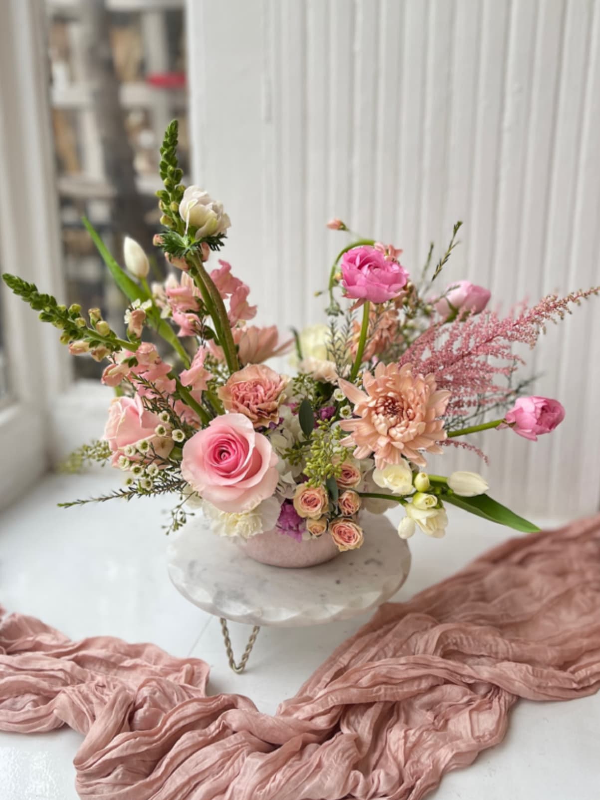 Pink and peach floral arrangement in a low vase on a pedestal
