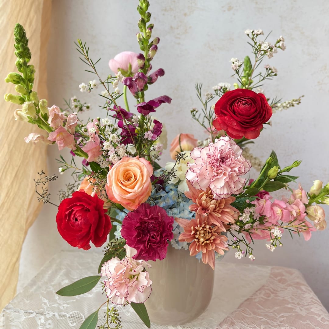 Mixed bouquet of roses, carnations, and snapdragons in a white vase