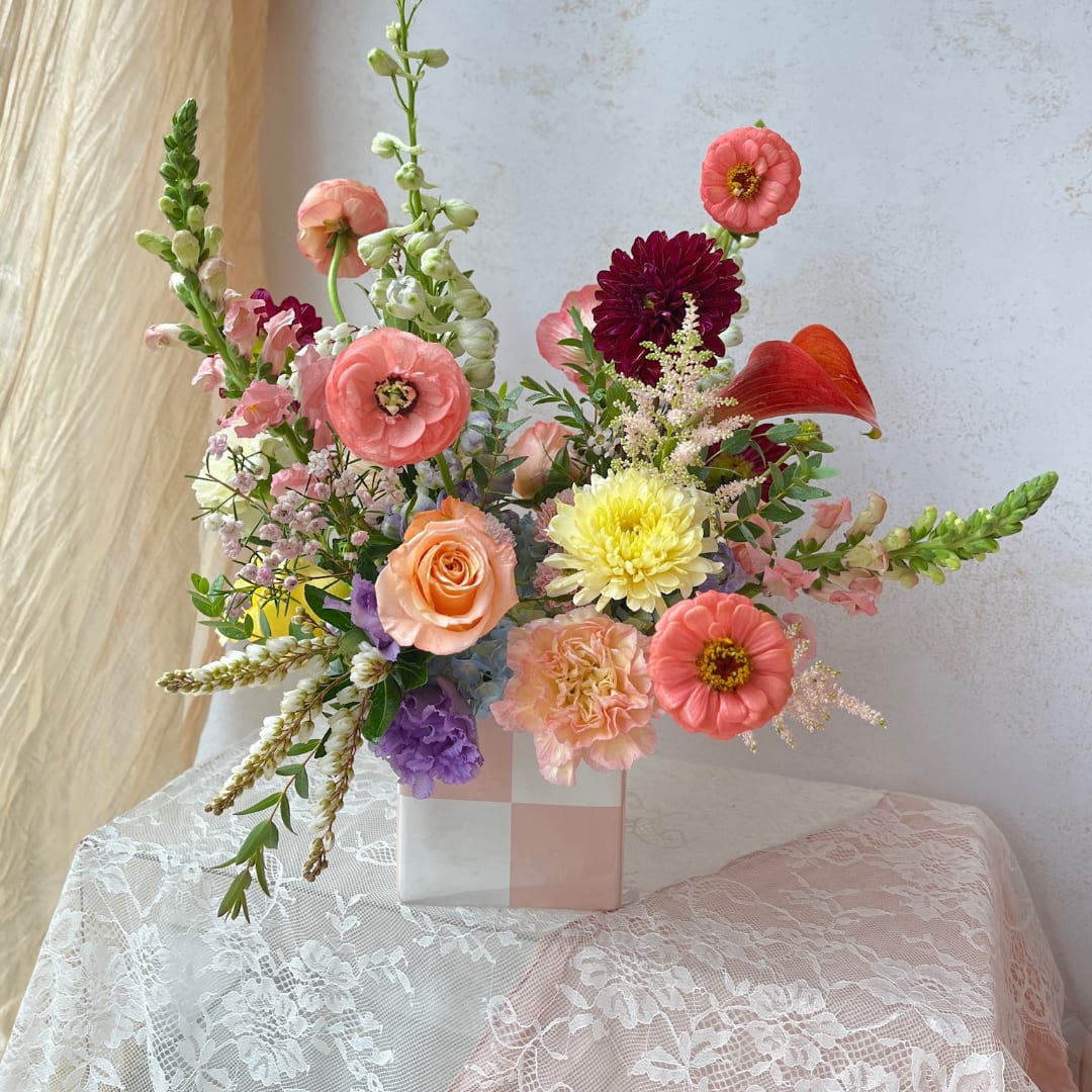 Mixed bouquet in a pink-and-white vase with coral, yellow, and purple flowers