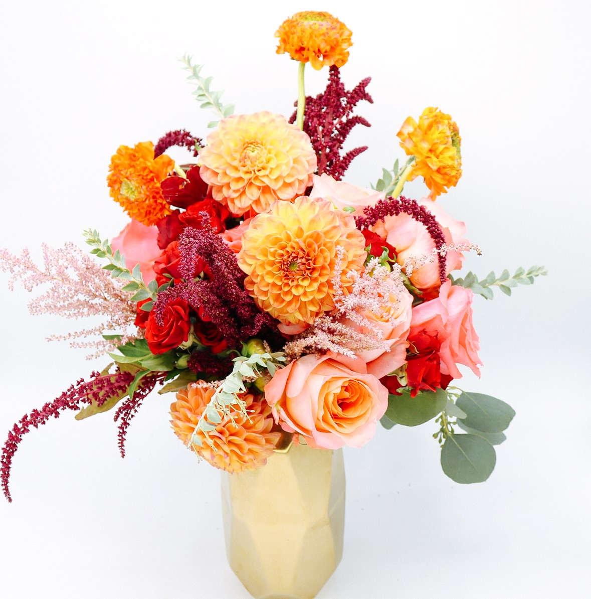 Bouquet of orange, pink, and red flowers in a gold vase