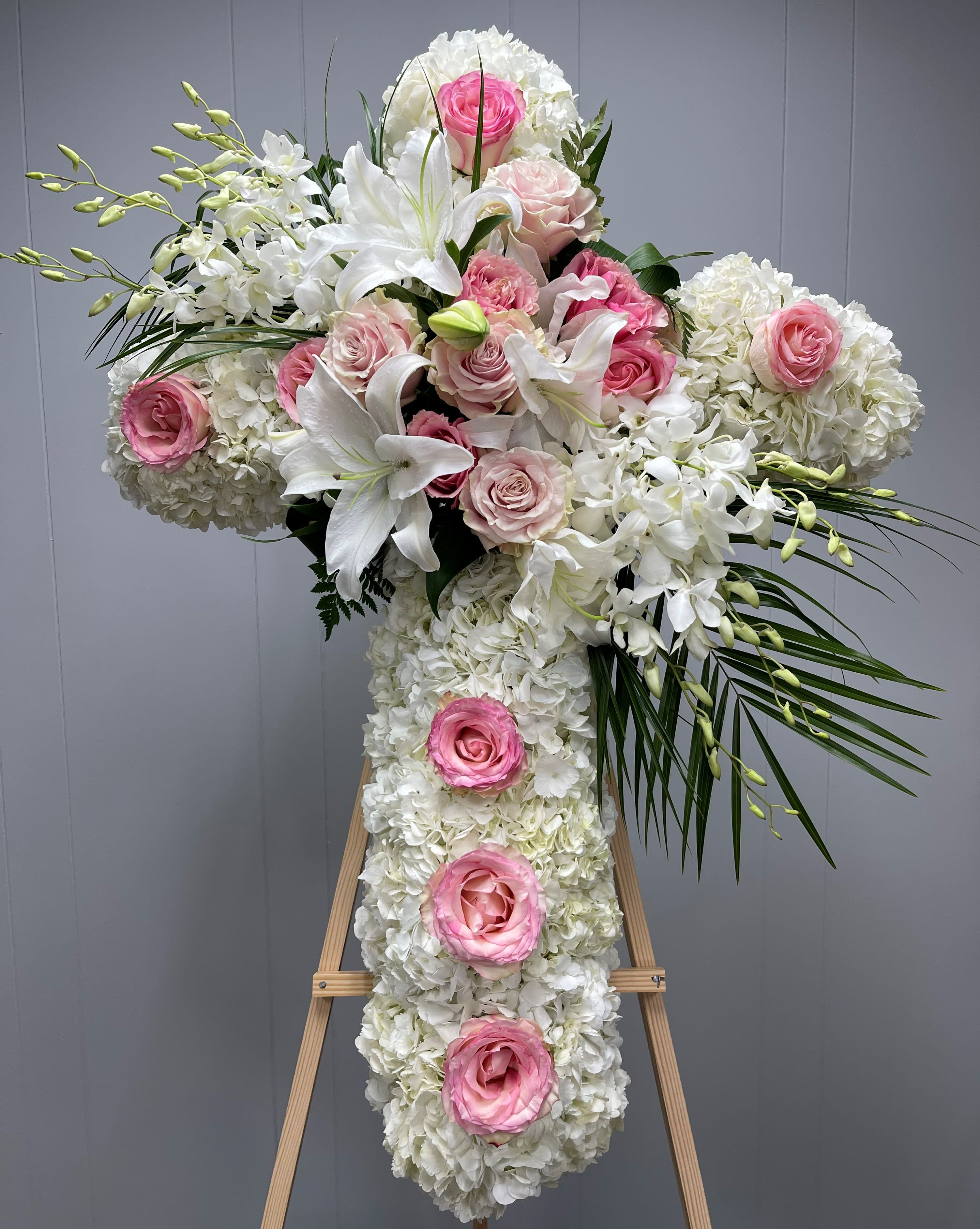 Large white floral cross with pink roses on an easel