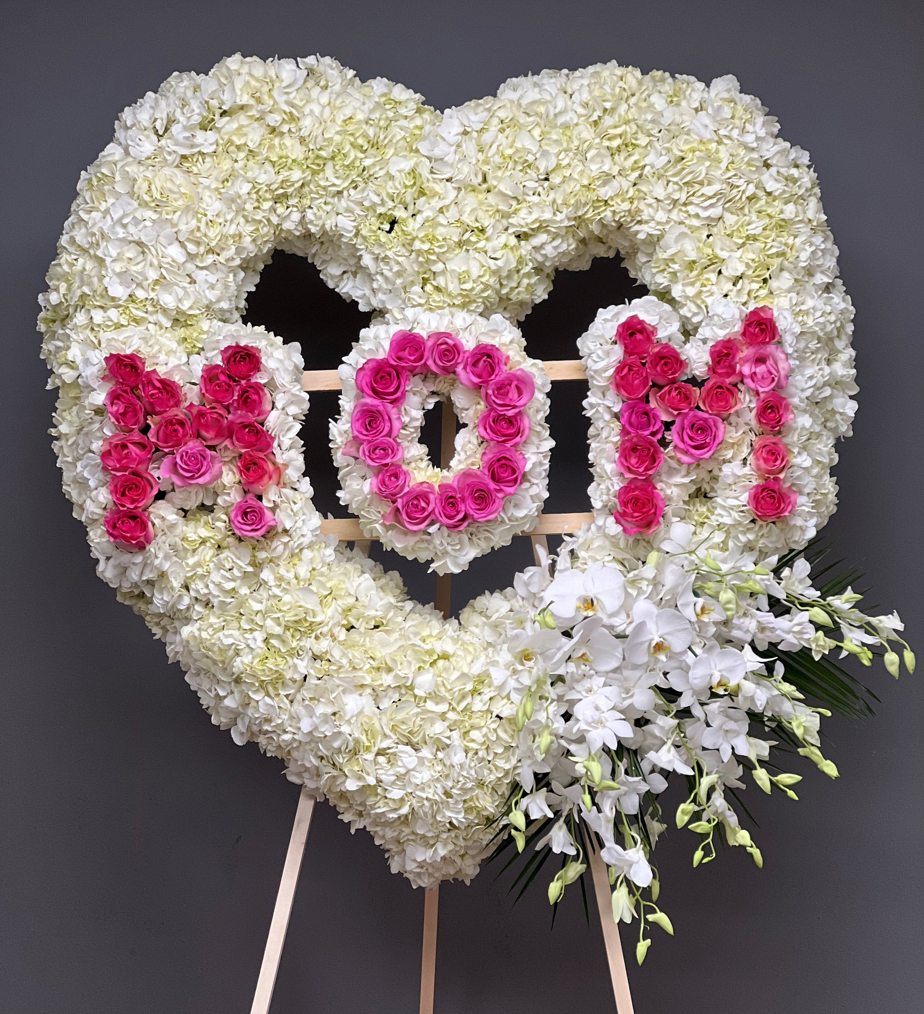 Heart-shaped floral tribute with white hydrangeas, pink roses, and white orchids on an easel