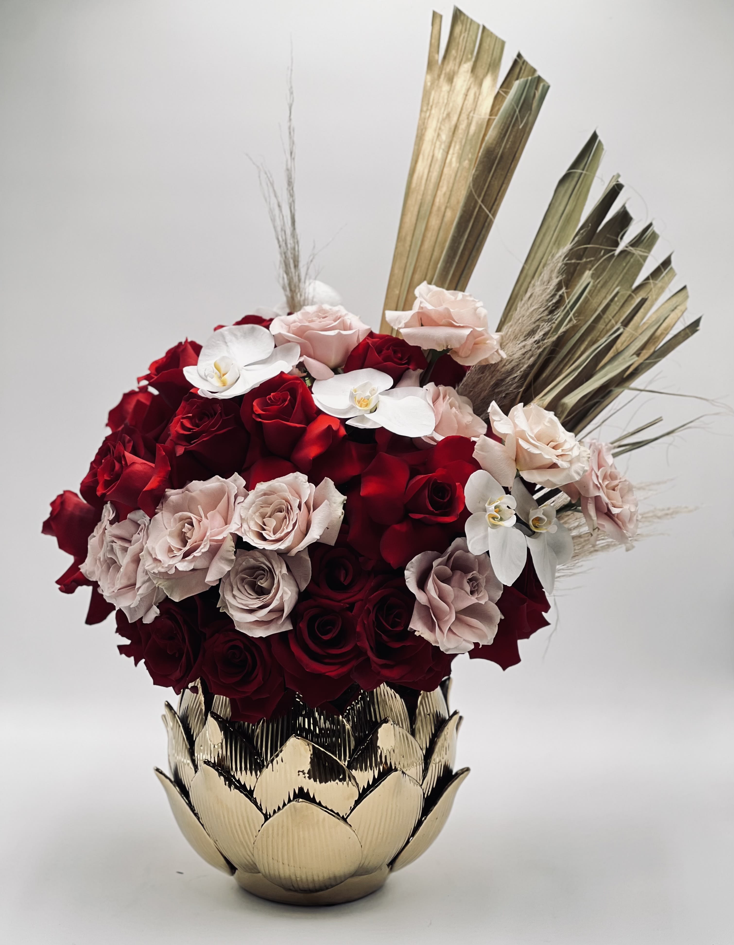 Red and blush roses arranged in a gold vase with white orchids
