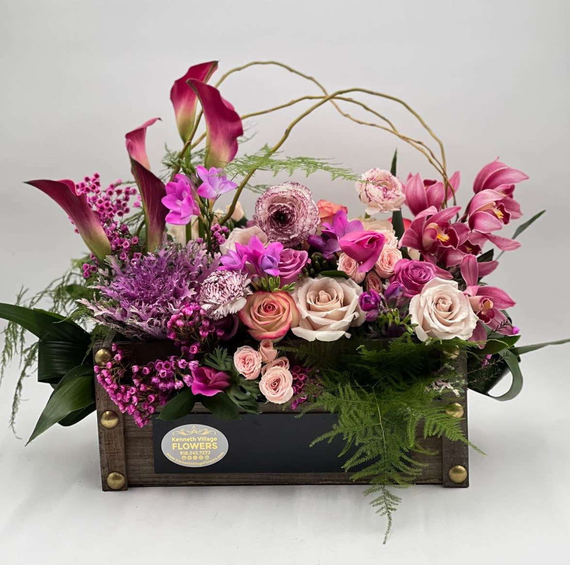 Pink and purple floral arrangement in a wooden box with roses and calla lilies