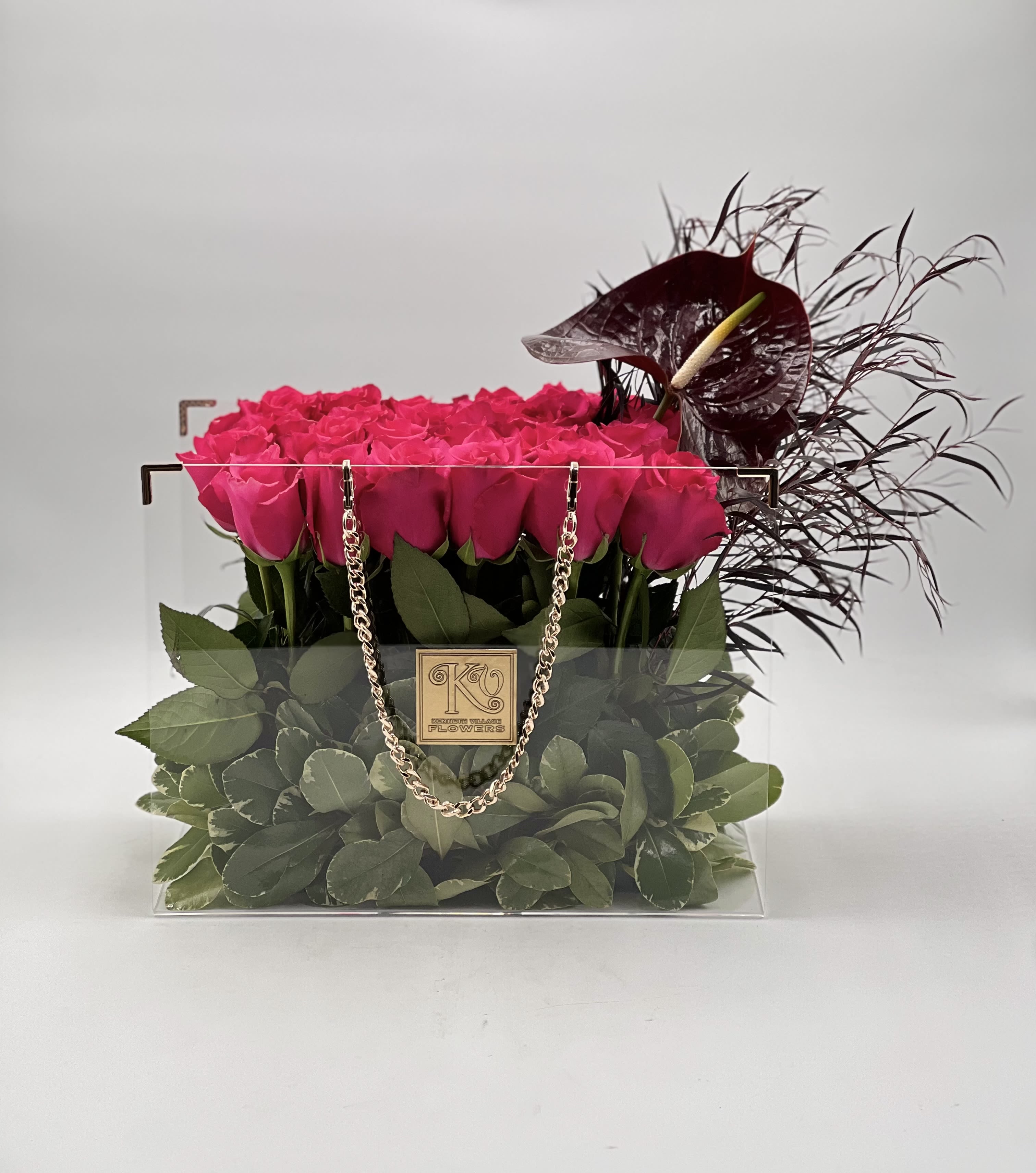 Pink roses in a clear square box with dark decorative flowers