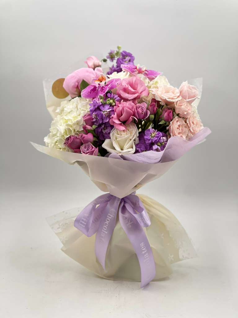 Soft Romance Bouquet - A hand-tied bouquet in soft lavender, blush pink, and creamy white tones, featuring seasonal accent blooms. Wrapped in an elegant  paper with a satin ribbon, this bouquet is a beautiful choice for birthdays, anniversaries, thank-you gifts, or any celebration.