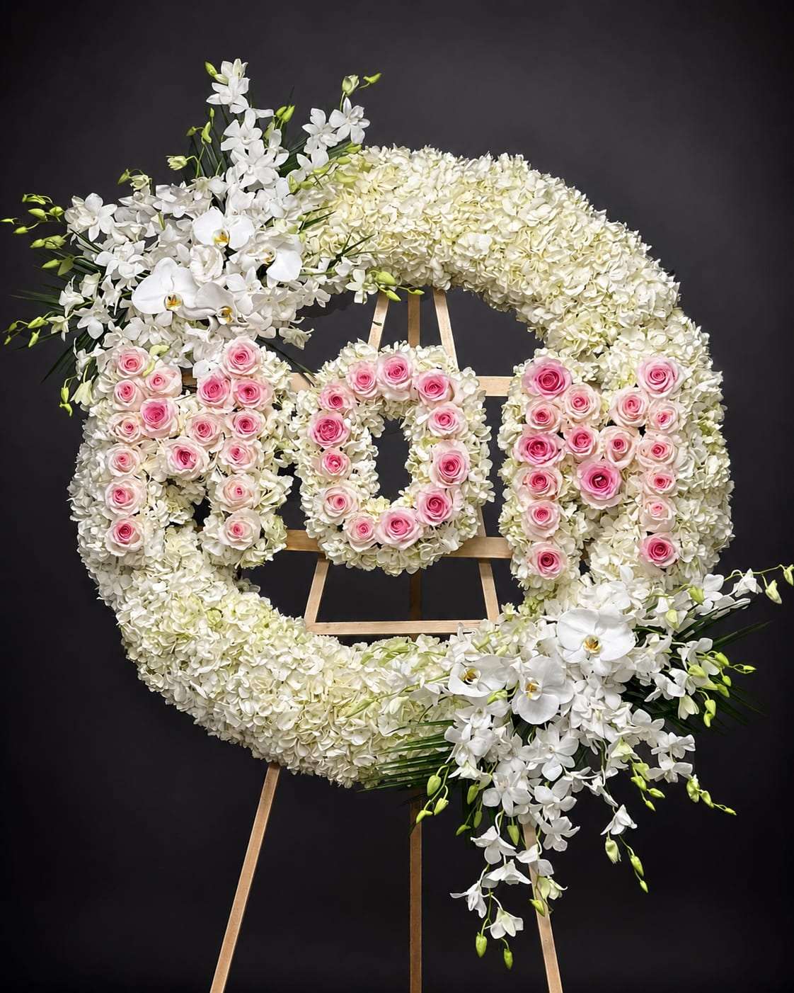 Large round spray with letters - This luxurious premium size round spray is designed as an addition to any memorial service. This arrangement highlights white hydrangeas that will ease the minds and comfort the souls that are grieving with Dendrobium and Phalaenopsis orchids and roses to represent the vibrance of their life. Colors are adjustable by request. The price includes printed ribbon or sympathy card. The diameter for this arrangement measures more than 40 inches.