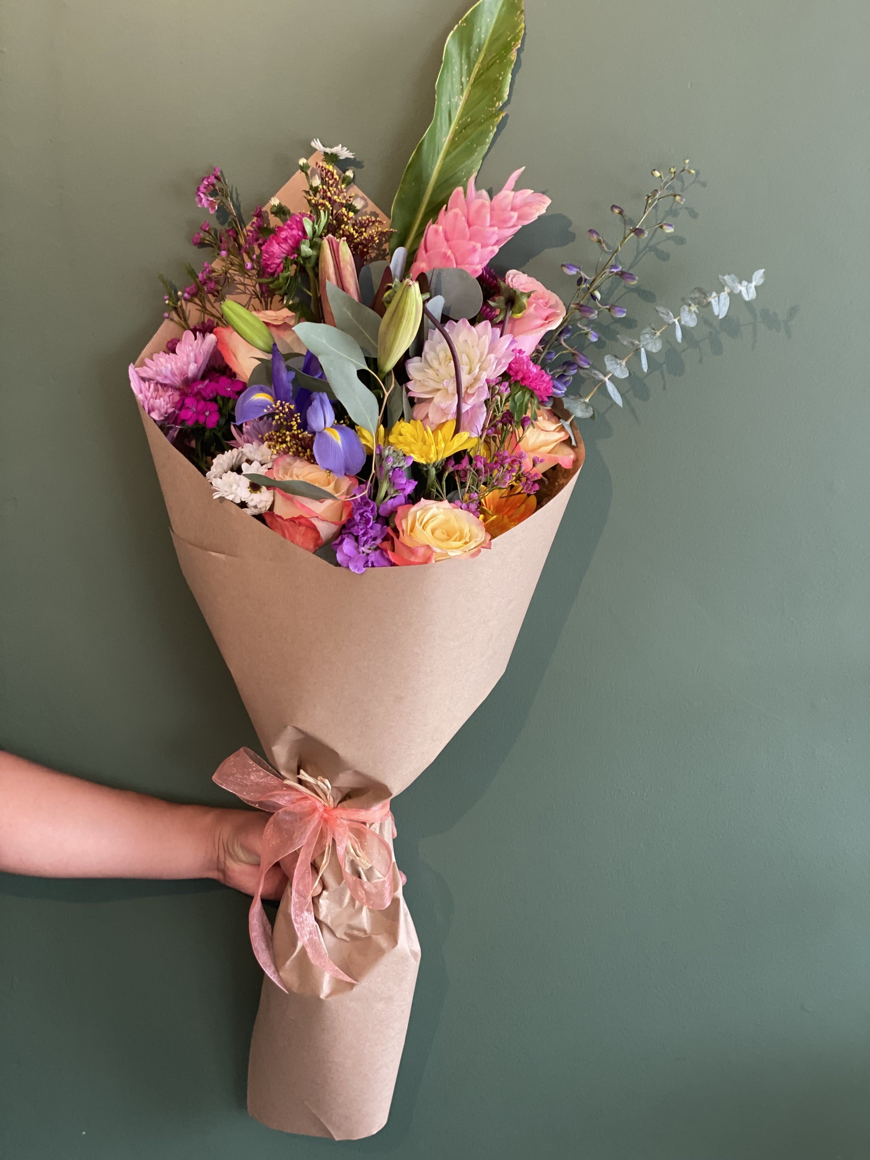 Colorful mixed flower bouquet wrapped in brown paper with a pink ribbon