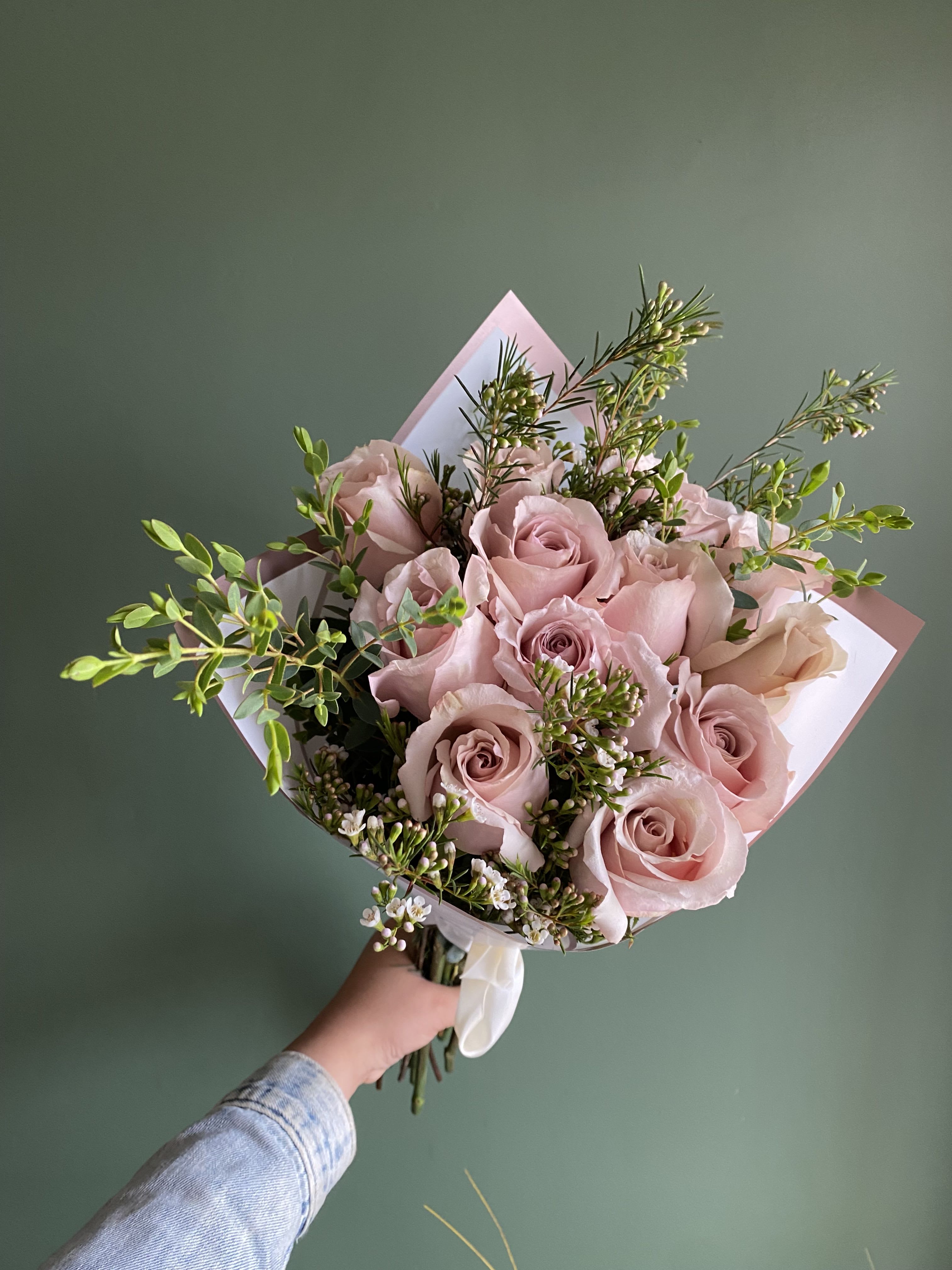 Handheld bouquet of pale pink roses with small white filler flowers
