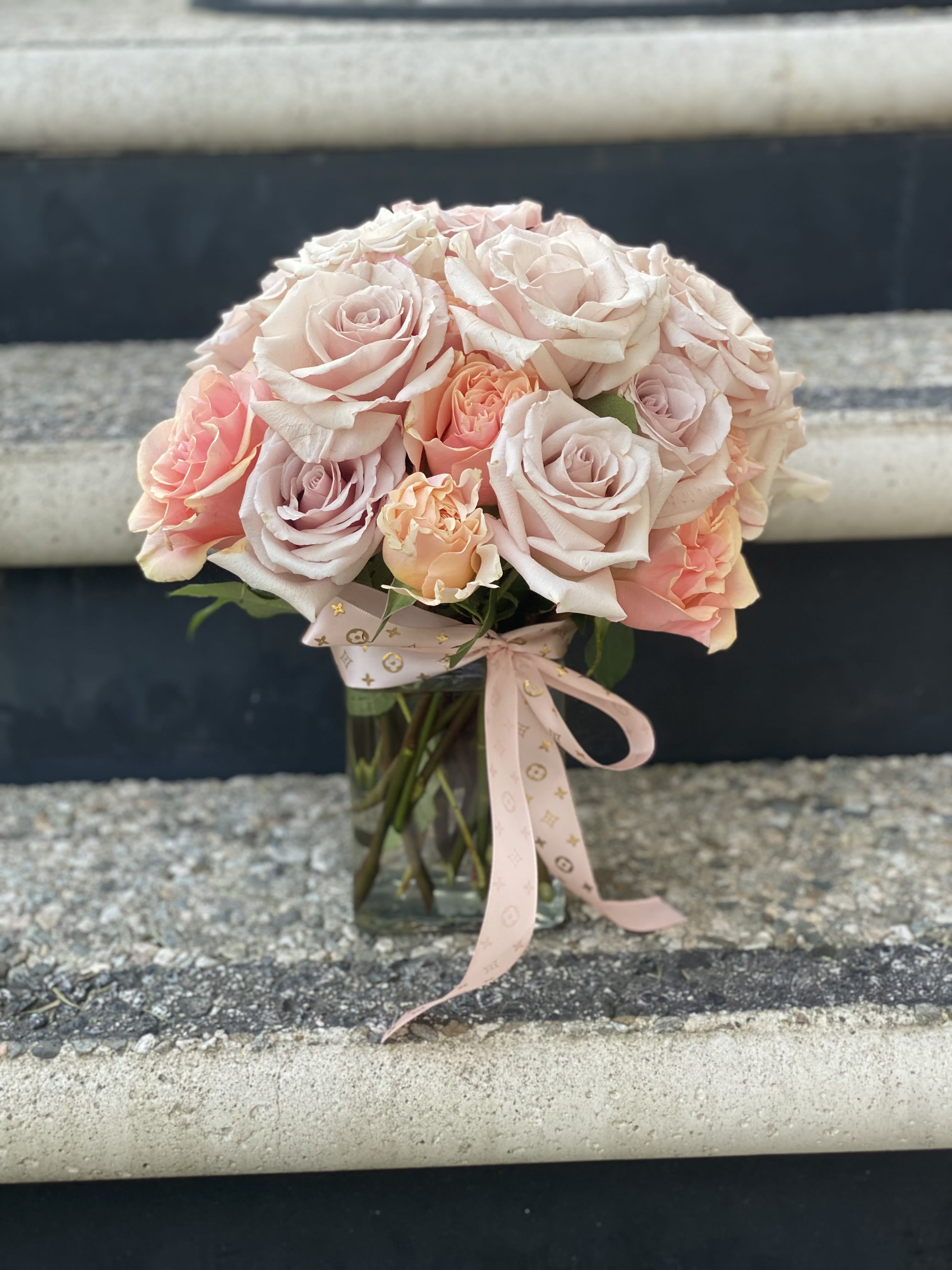 Bouquet of pale pink and peach roses in a clear glass vase with a ribbon