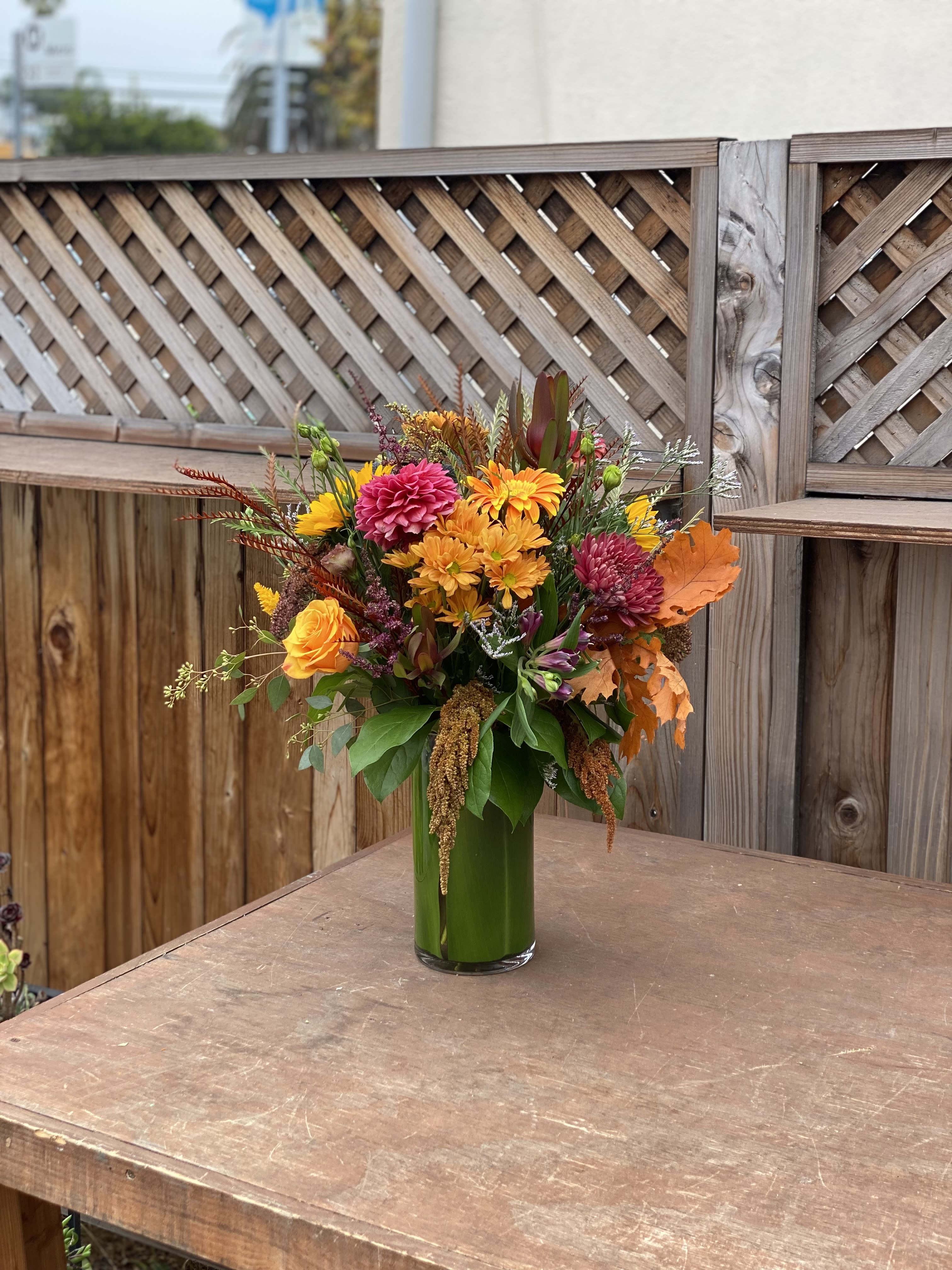 Autumn bouquet of orange, yellow, and pink flowers in a tall glass vase