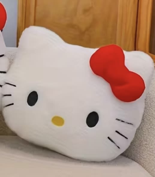 Hello Kitty plush pillow with a red bow on a bed